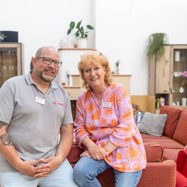 Ein Mann und eine Frau lehnen auf einer roten Couch und schauen in die Kamera.