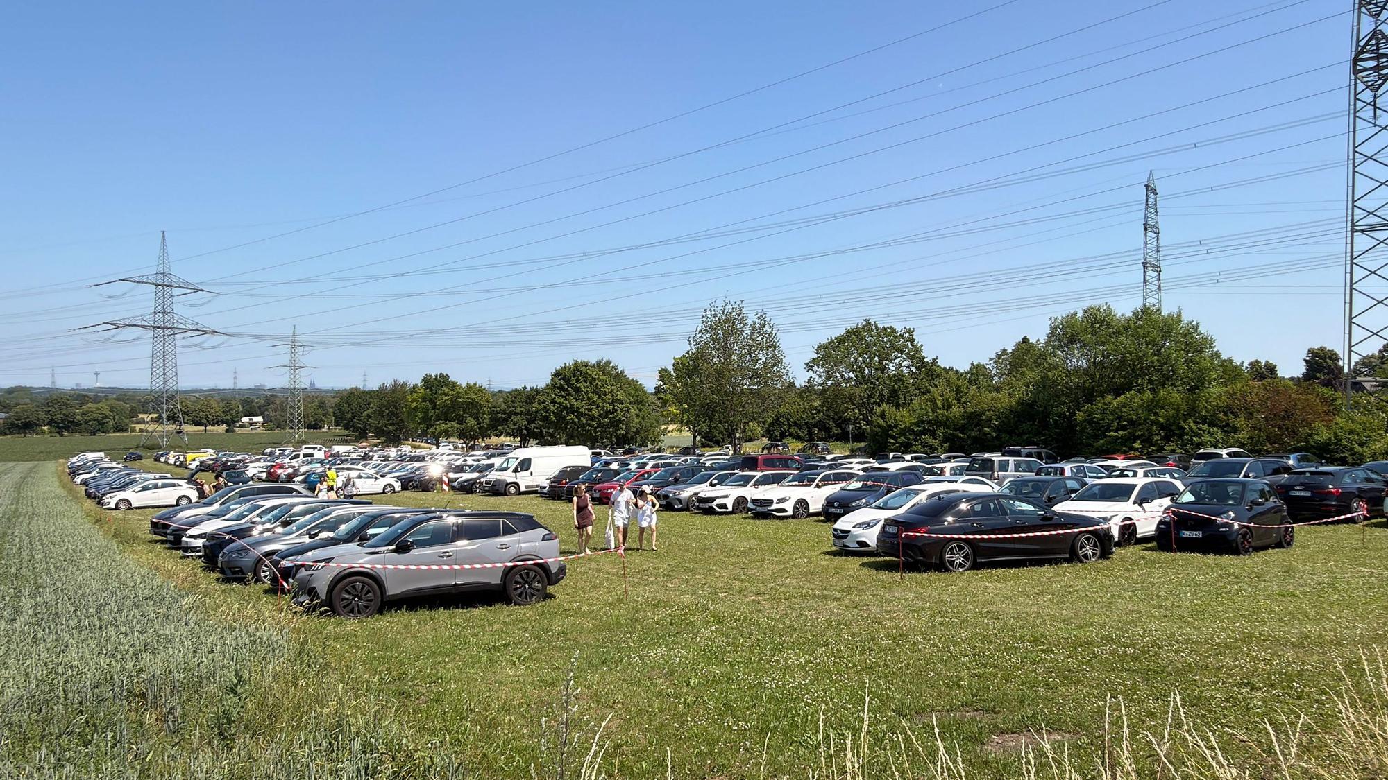Auf dem Bild ist ein voller Parkplatz auf einer Wiese zu sehen.
