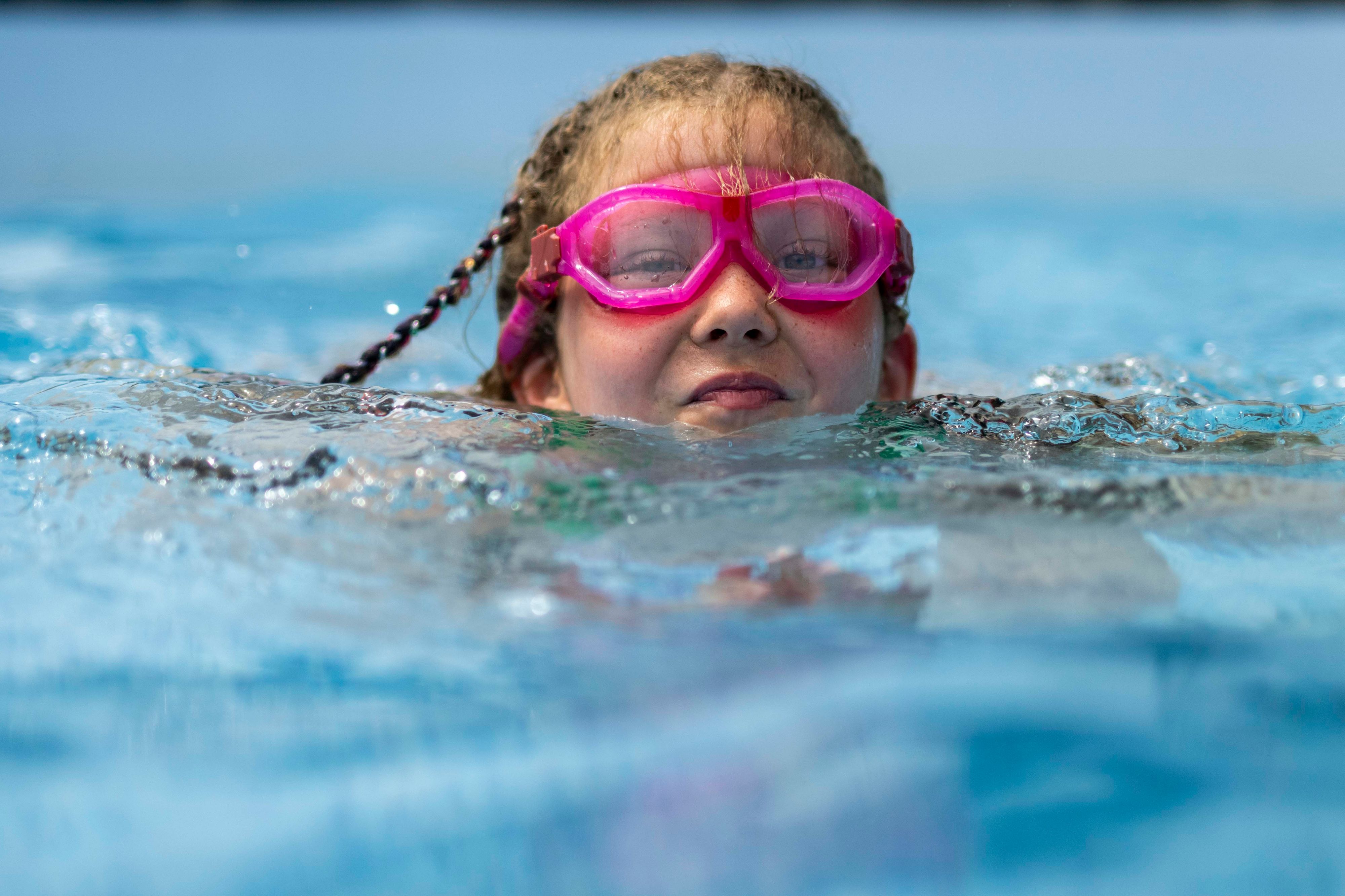 Ein Kind mit rosa Brille schwimmt im Wasser.