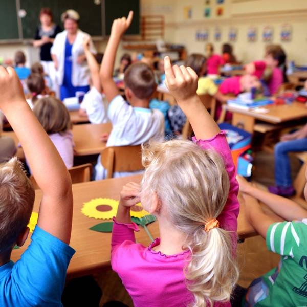 Kinder sitzen an Holztischen in einem Klassenraum.