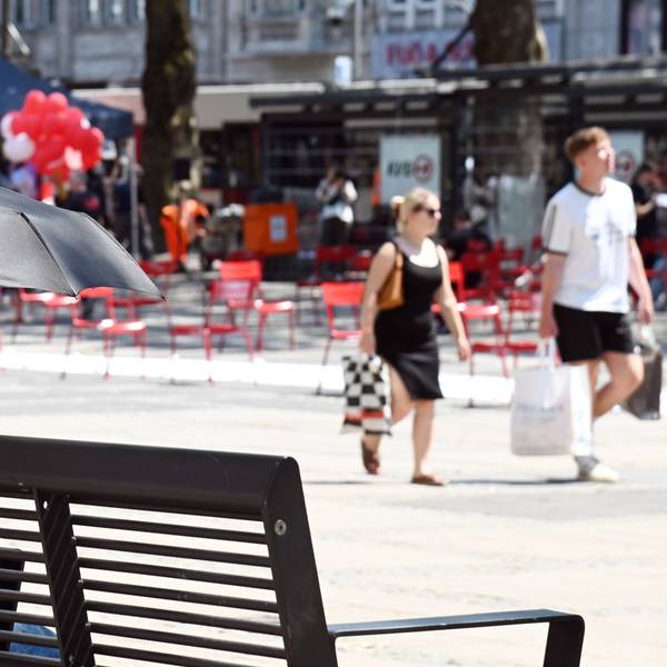 Eine Frau sitzt mit einem Schirm zum Schutz vor der Sonne auf einer Bank am Neumarkt.