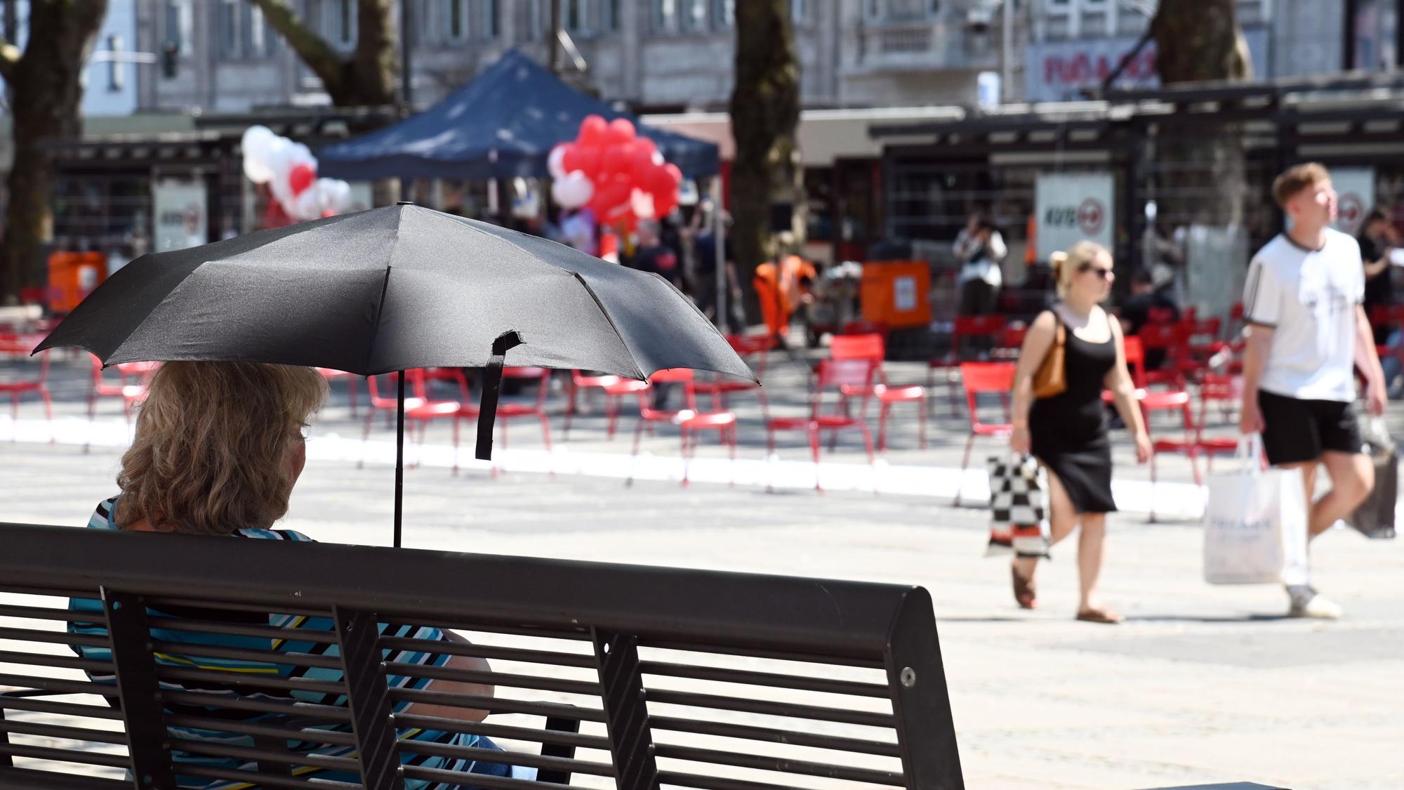 Eine Frau sitzt mit einem Schirm zum Schutz vor der Sonne auf einer Bank am Neumarkt.