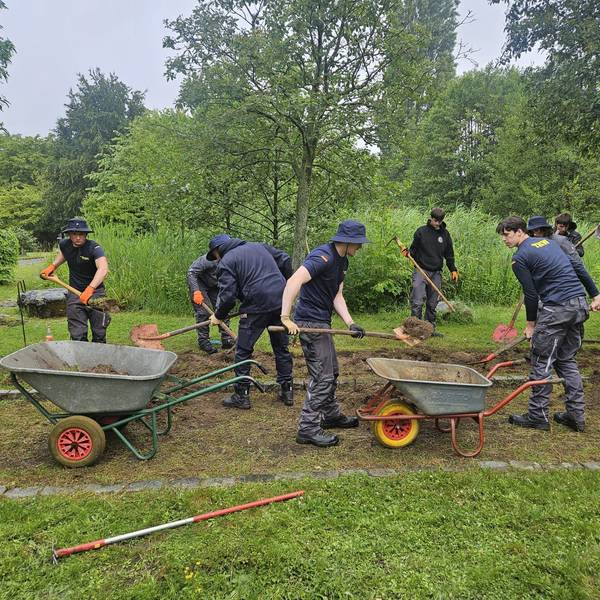 Mehrere Männer arbeiten mit Schaufeln in einer Grünanlage. Sie haben auch zwei Schubkarren dabei.
