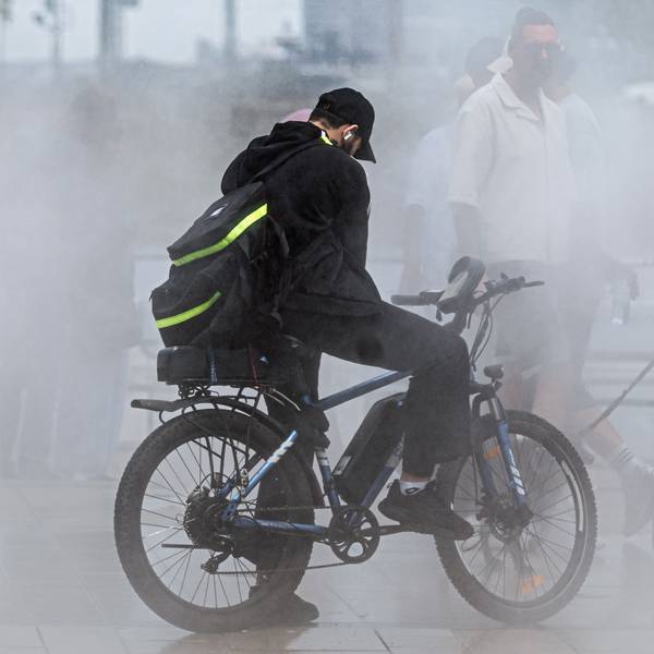 Passanten suchen bei einer Temperatur um 33 Grad Abkühlung auf einer Sprühnebelanlage.