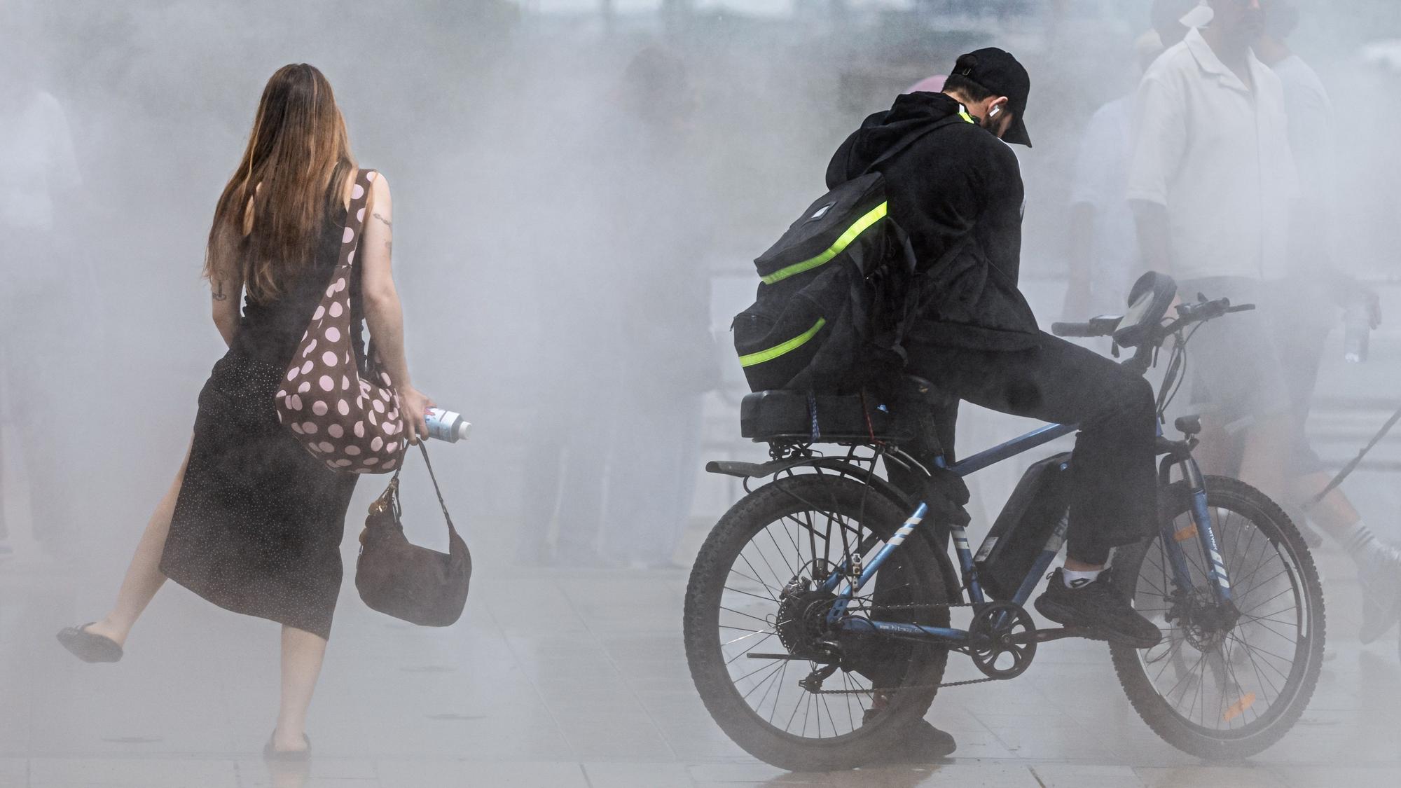 Passanten suchen bei einer Temperatur um 33 Grad Abkühlung auf einer Sprühnebelanlage.