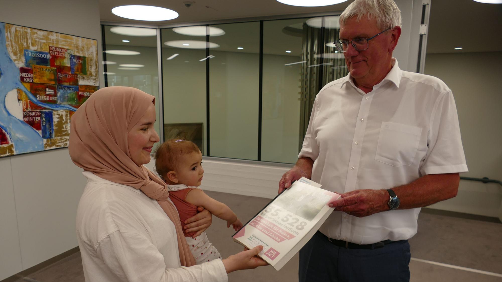 Naima Farhane, mit der kleinen Aischa auf dem Arm, übergibt Landrat Sebastian Schuster die Petition mit 35.528 Unterschriften.