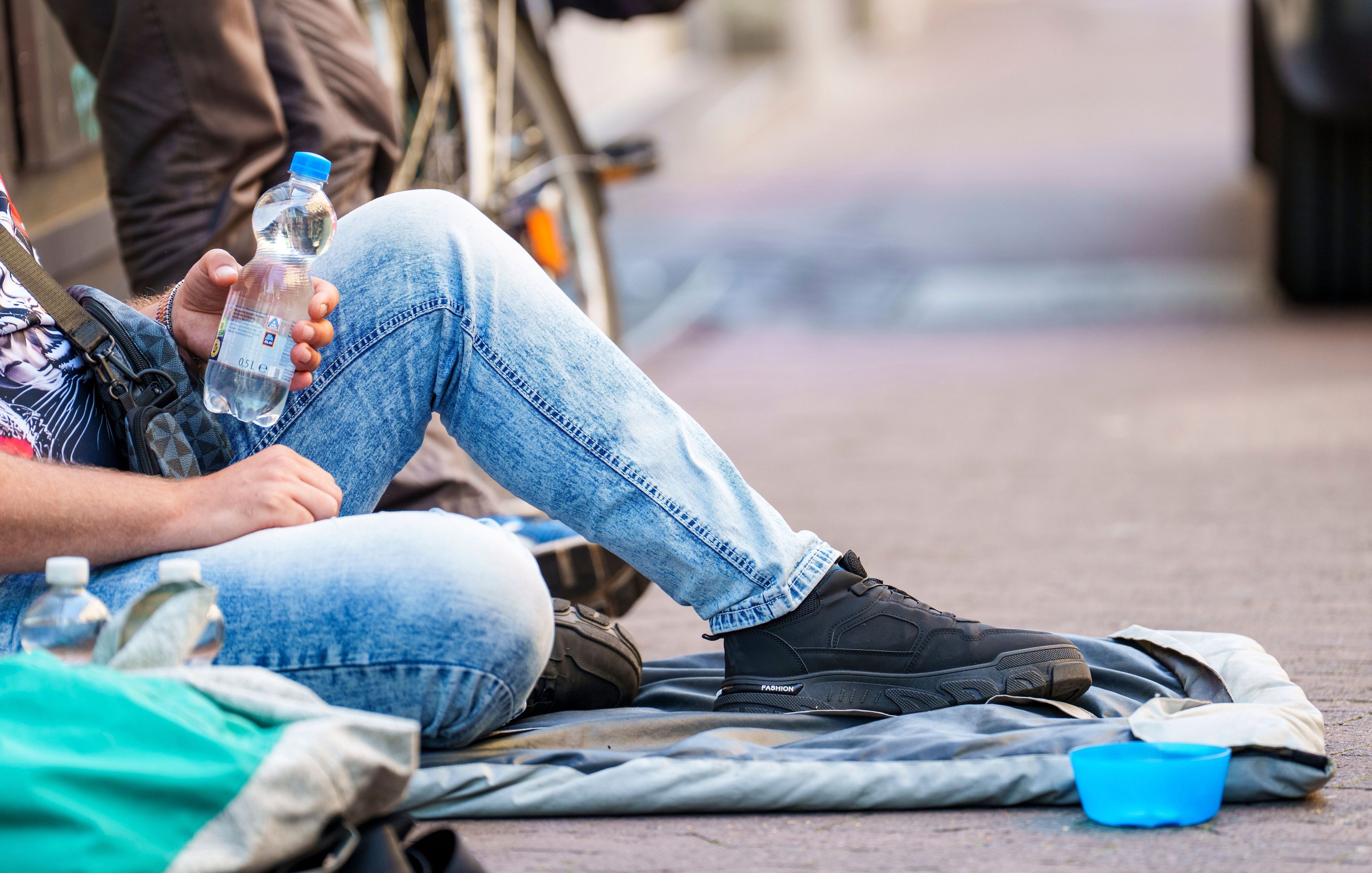 Ein Obdachloser sitzt in der Innenstadt und hält eine Wasserflasche in der Hand.