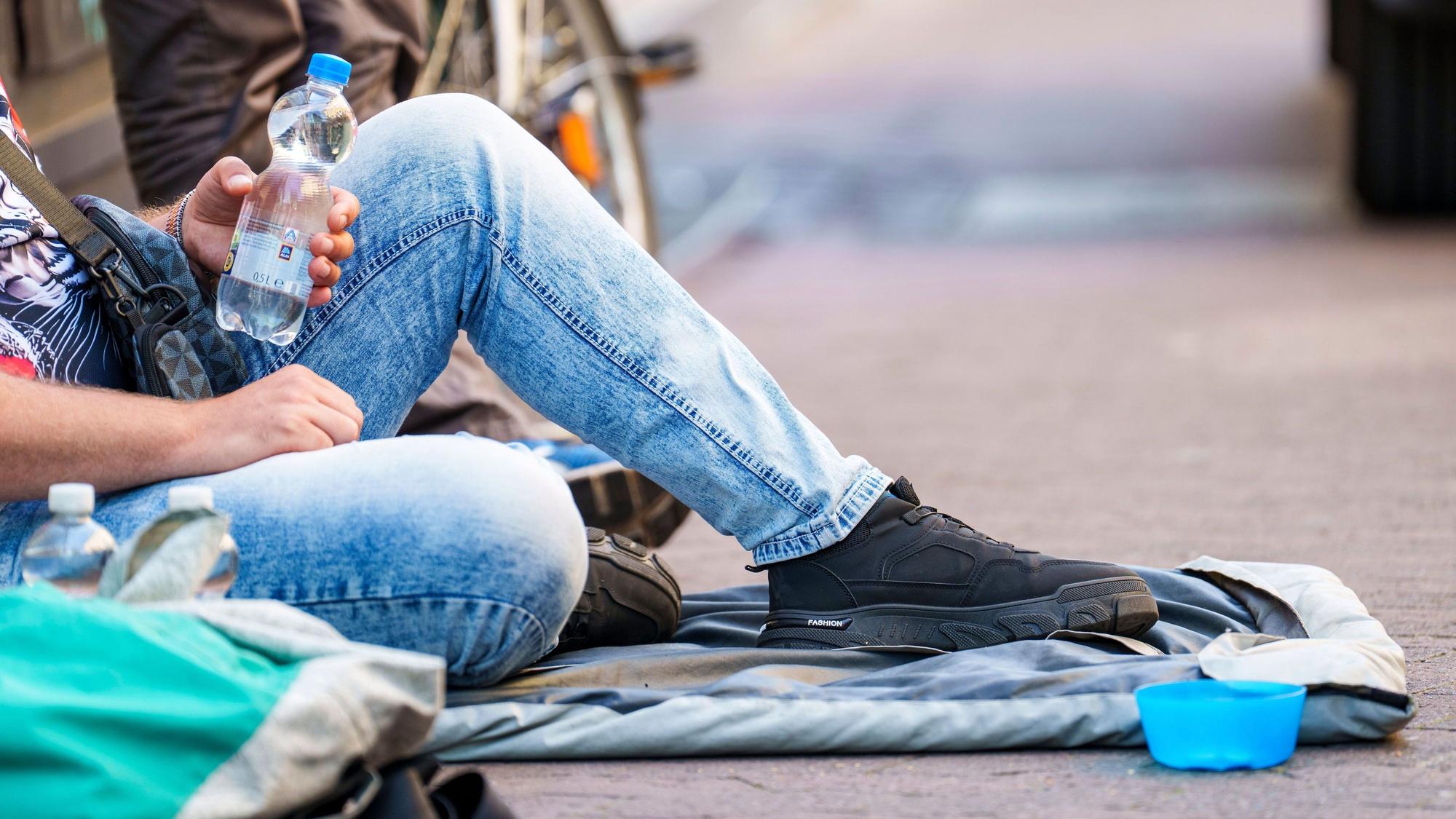 Ein Obdachloser sitzt in der Innenstadt und hält eine Wasserflasche in der Hand.