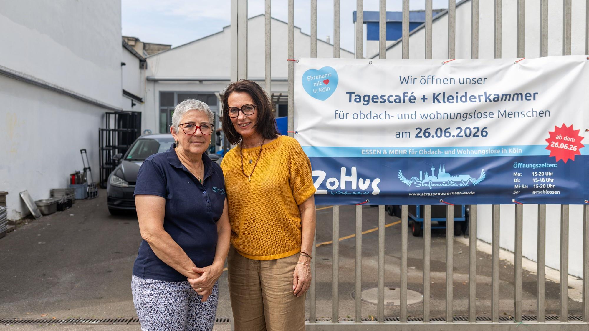 Zwei Frauen stehen vor einem Gitterzaun und schauen in die Kamera.