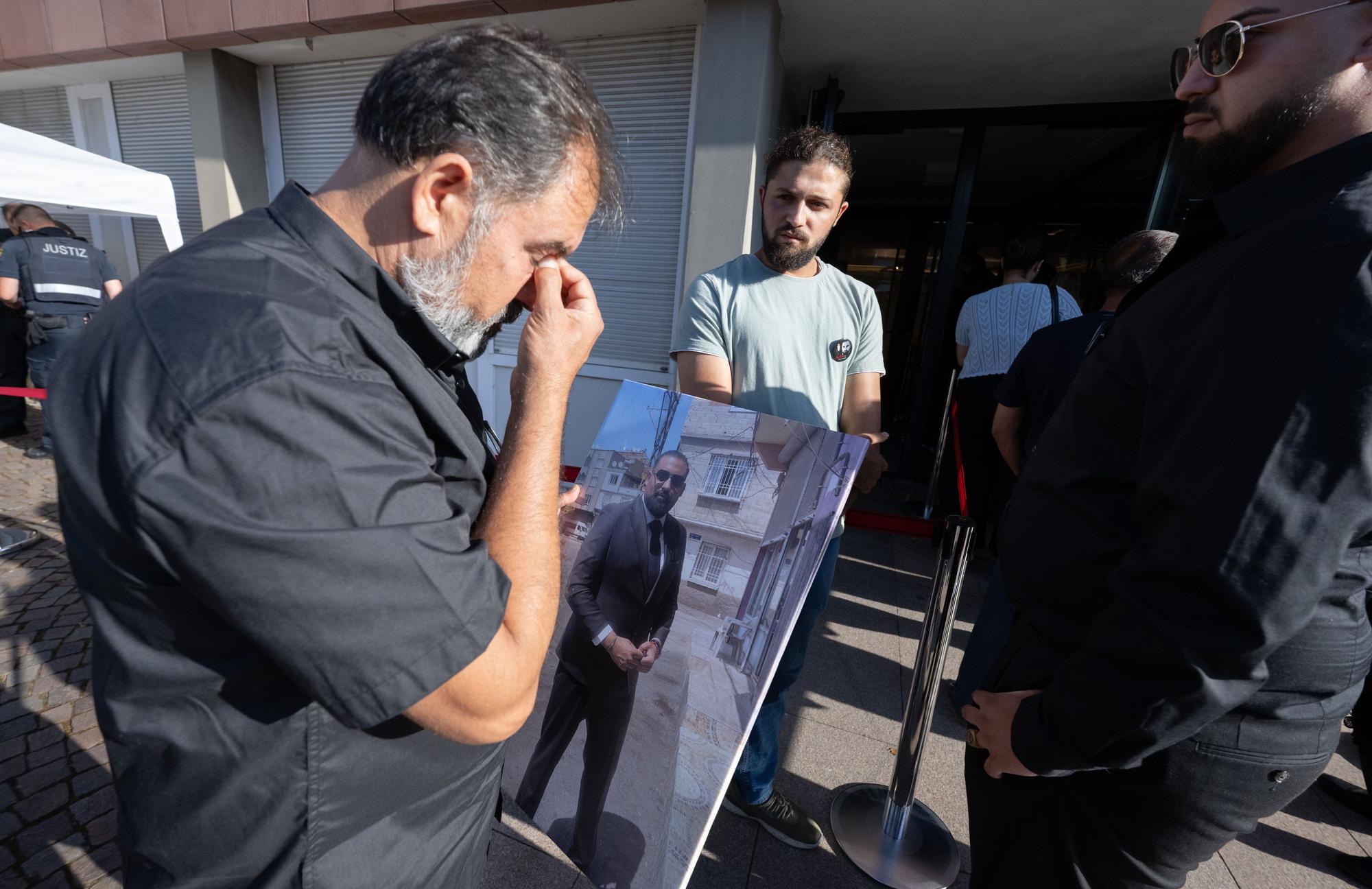 24.06.2026, Rheinland-Pfalz, Zweibrücken: Weinend wartet Erdal Calar, Vater des getöteten Zugbegleiters Serkan Calar mit einem Bild seines Sohnes in der Hand auf Einlass in das Landgericht. Foto: Boris Roessler/dpa +++ dpa-Bildfunk +++