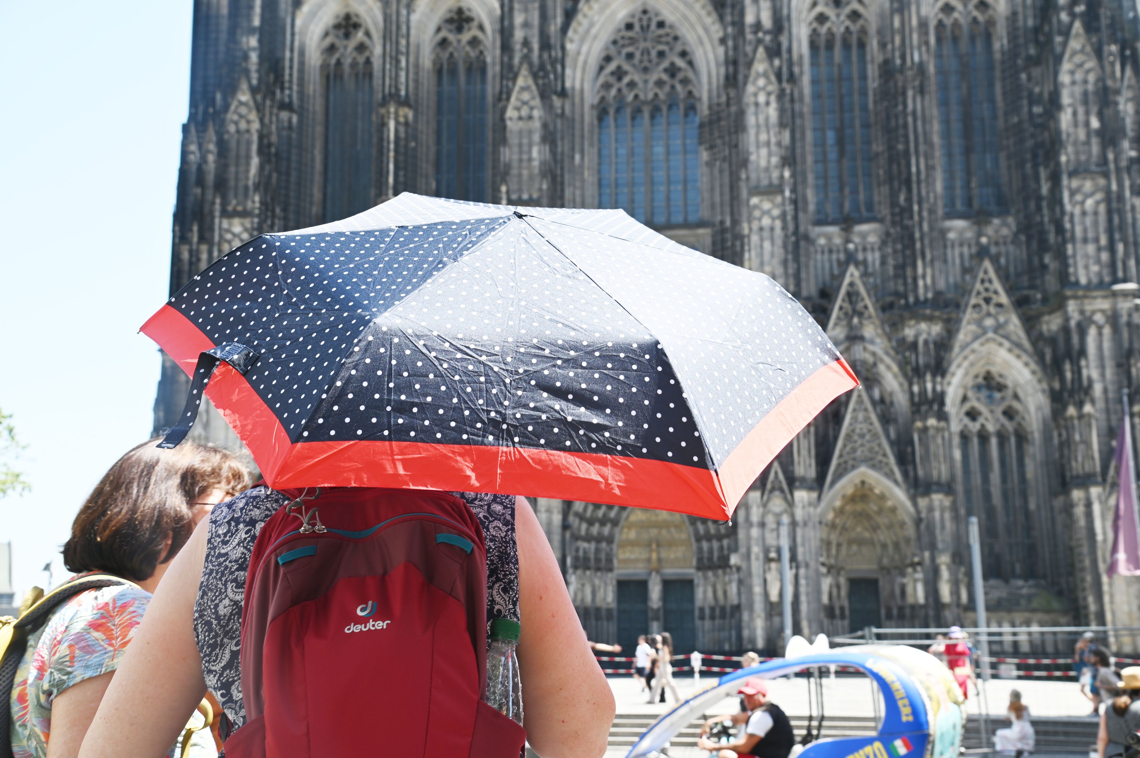 Eine Frau mit Regenschirm als Sonnenschutz vor dem Kölner Dom.