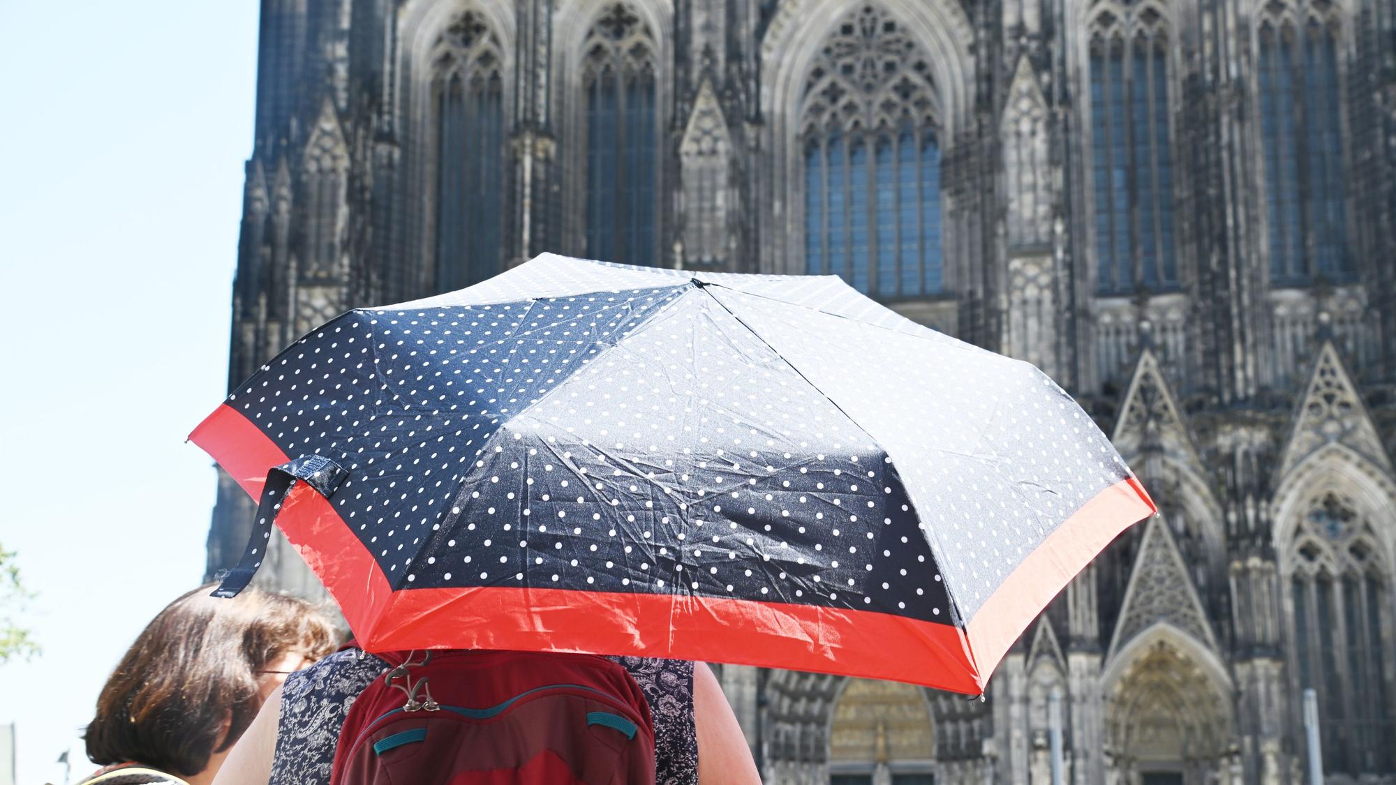 Eine Frau mit Regenschirm als Sonnenschutz vor dem Kölner Dom.