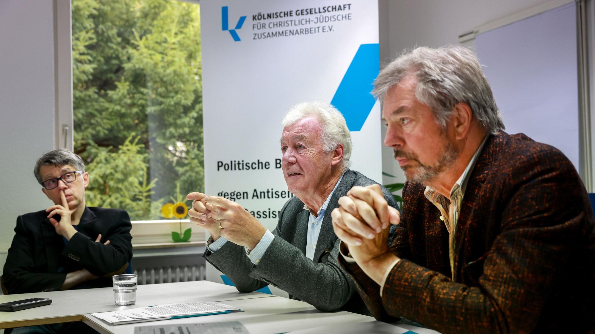 Jürgen Wilhlem sitzt bei einem Pressegsepräch an einem Tisch, im Hintergrund ist ein Aufsteller der Kölnischen Gesellschaft für Christlich-Jüdische Zusammenarbeit zu sehen.