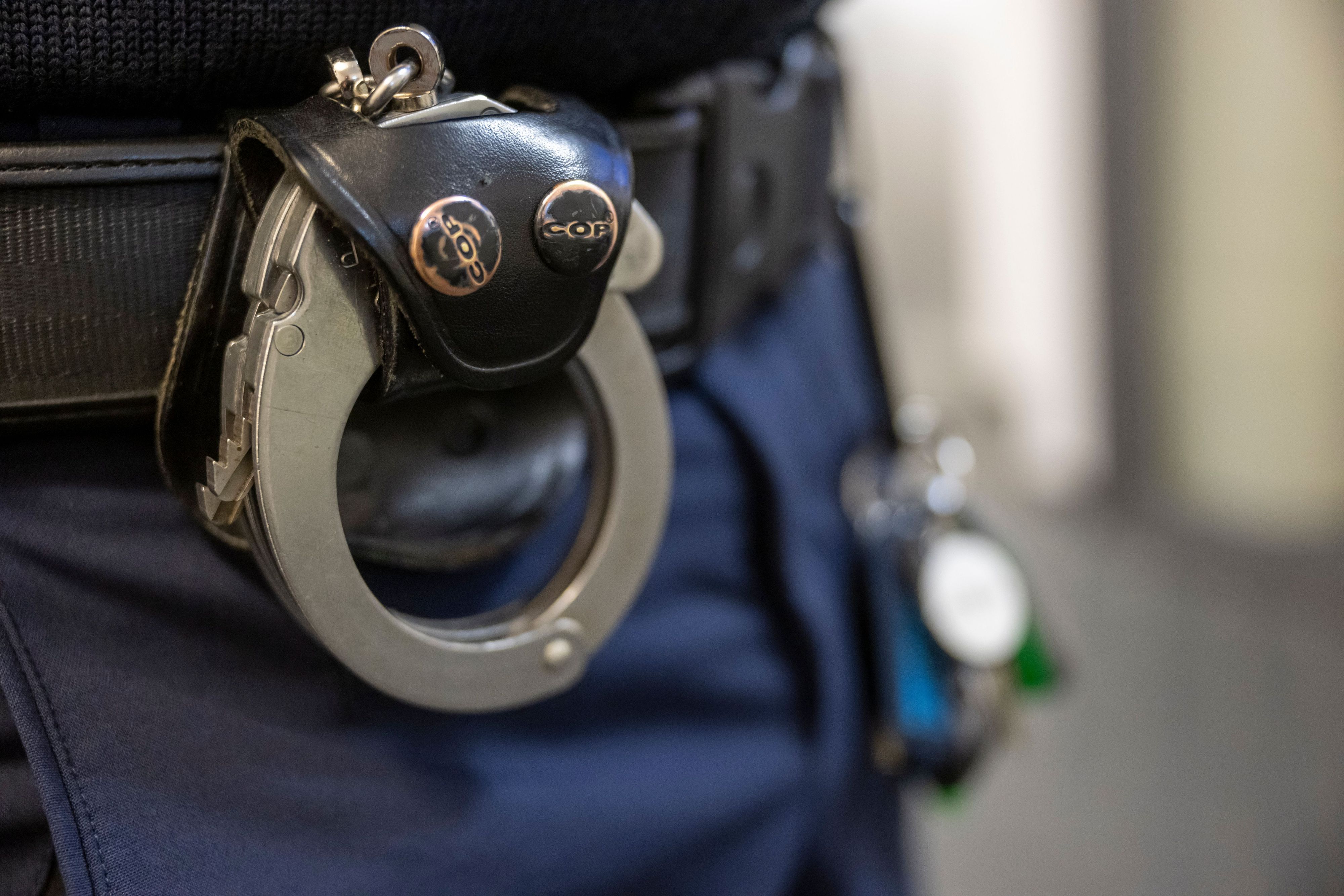 Eine Handschelle hängt am Gürtel eines Polizisten.