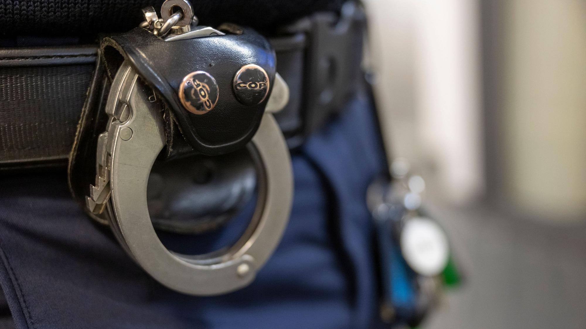 Eine Handschelle hängt am Gürtel eines Polizisten.