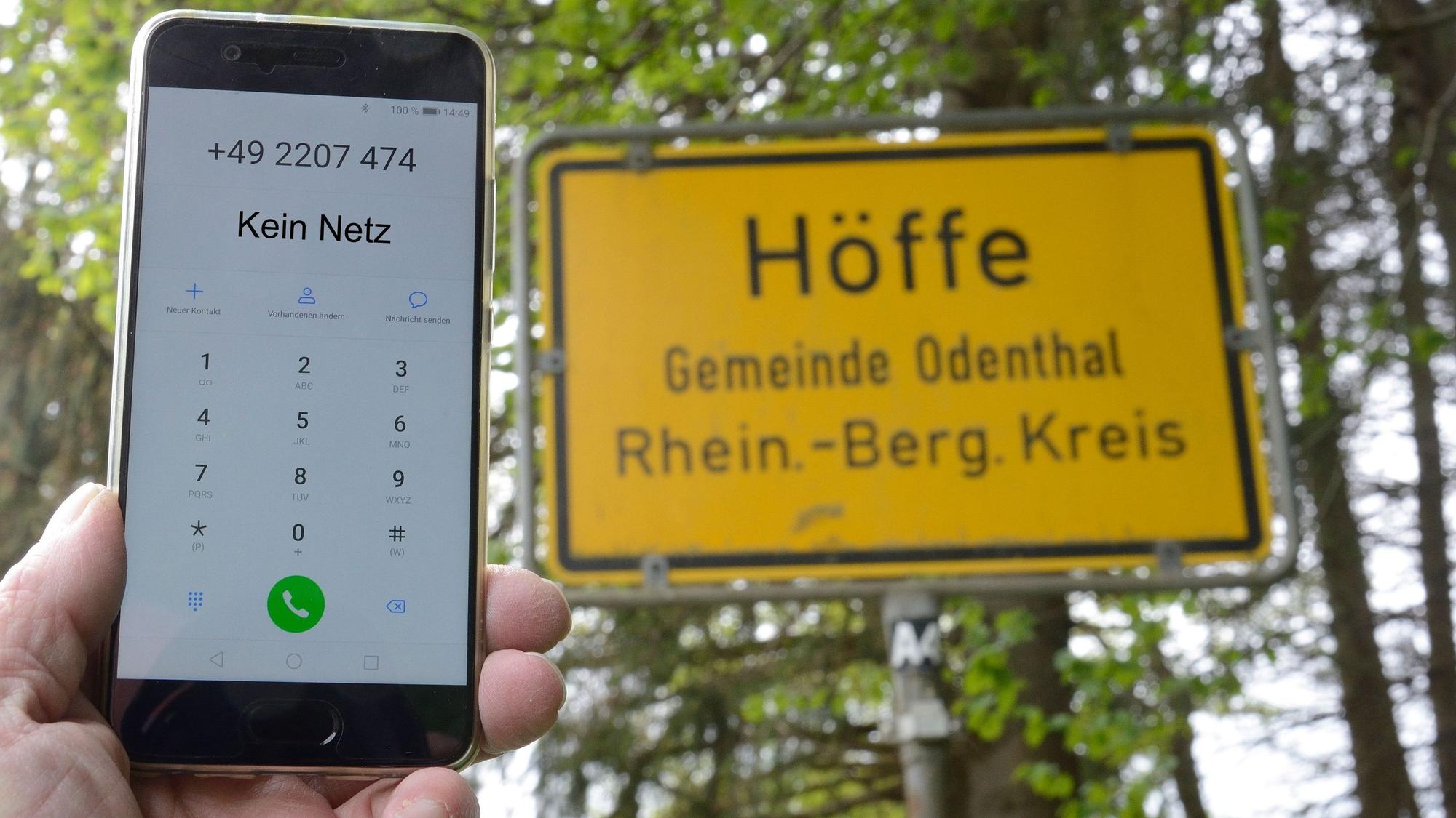 Jemand Halt ein Handy, das kein Netz hat, vor ein Ortschild in Odenthal.