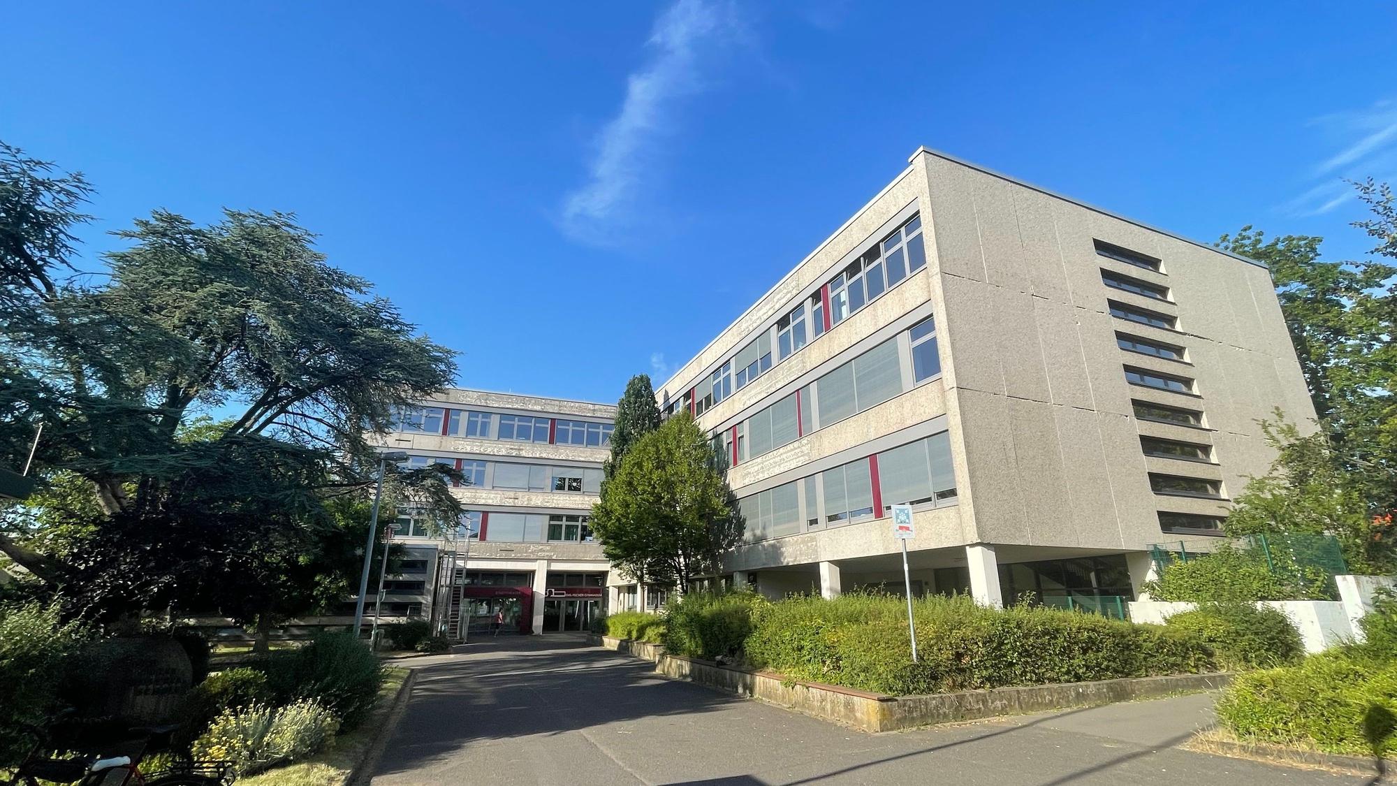 Blick auf das Schulgebäude, das von mehreren Bäumen flankiert wird.