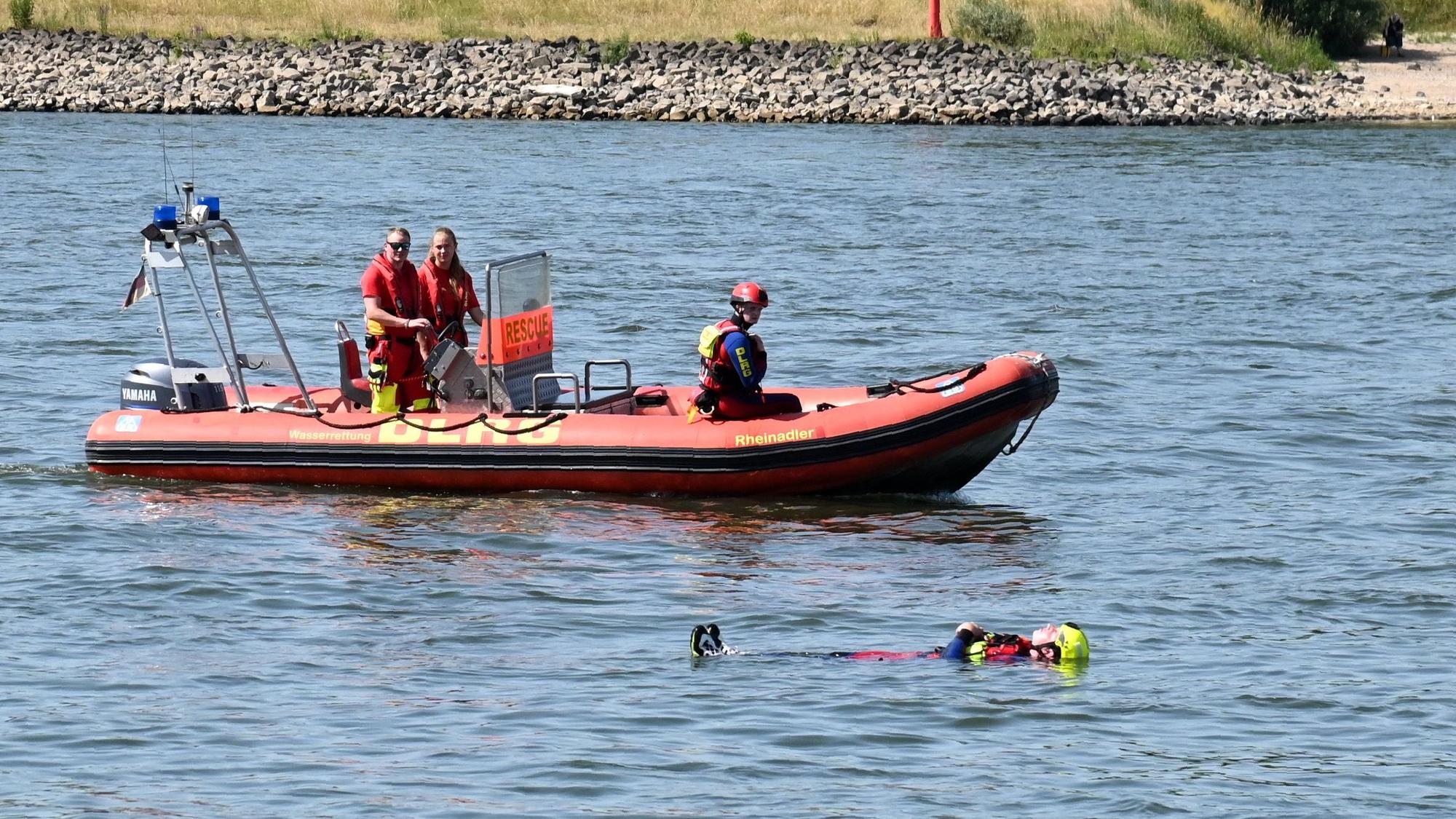 Ein Schwimmer der DLRG treibt neben einem Rettungsboot in Rückenlage auf dem Rhein.