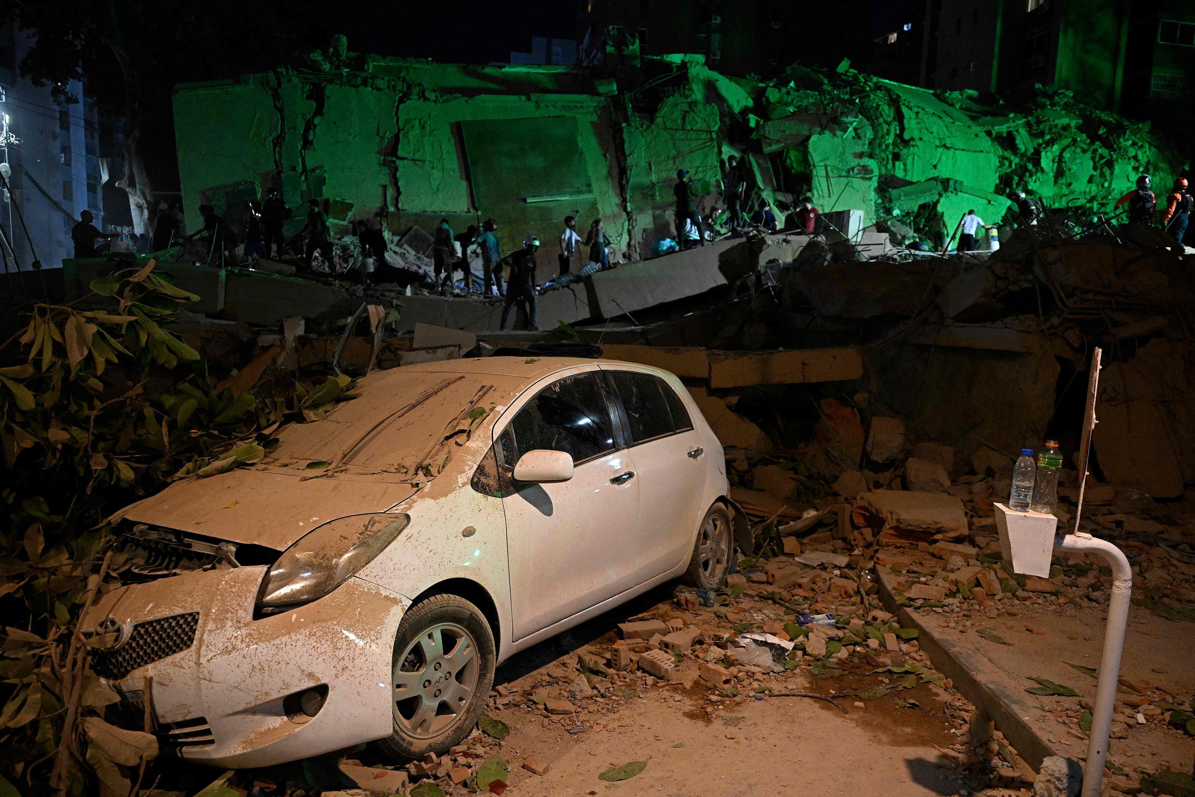 Ein von einem umgestürzten Baum zerstörtes Auto ist zu sehen, während Menschen nach dem Erdbeben in Caracas vor einem zerstörten Gebäude vorbeigehen.