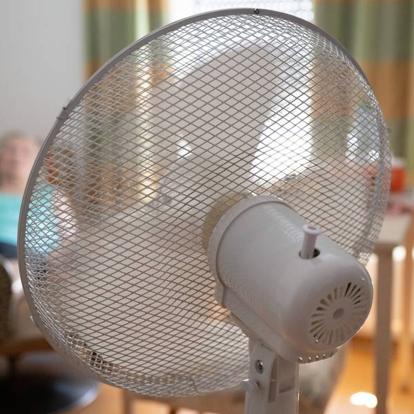 Die Bewohnerin eines Seniorenzentrums sitzt in ihrem Zimmer hinter einem Ventilator in einem Sessel.