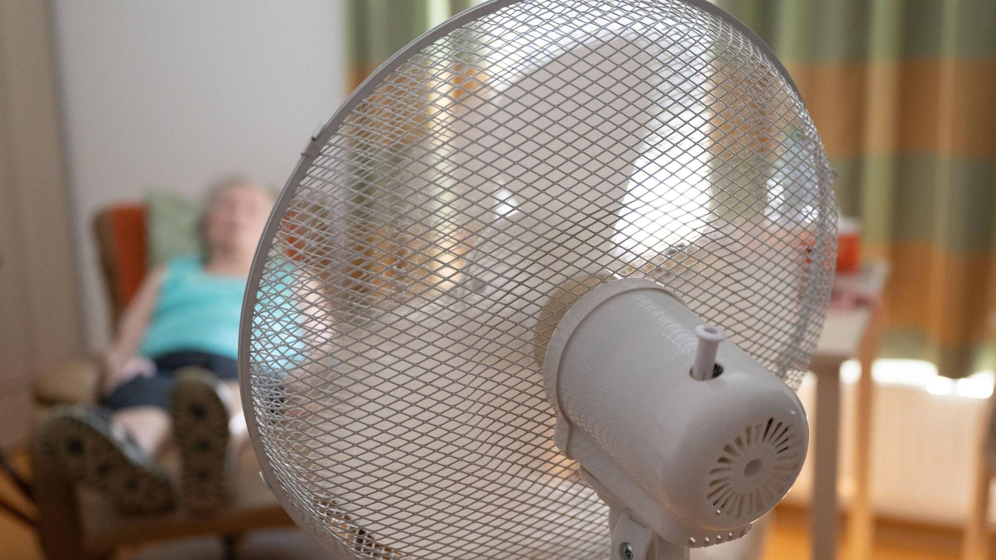 Die Bewohnerin eines Seniorenzentrums sitzt in ihrem Zimmer hinter einem Ventilator in einem Sessel.