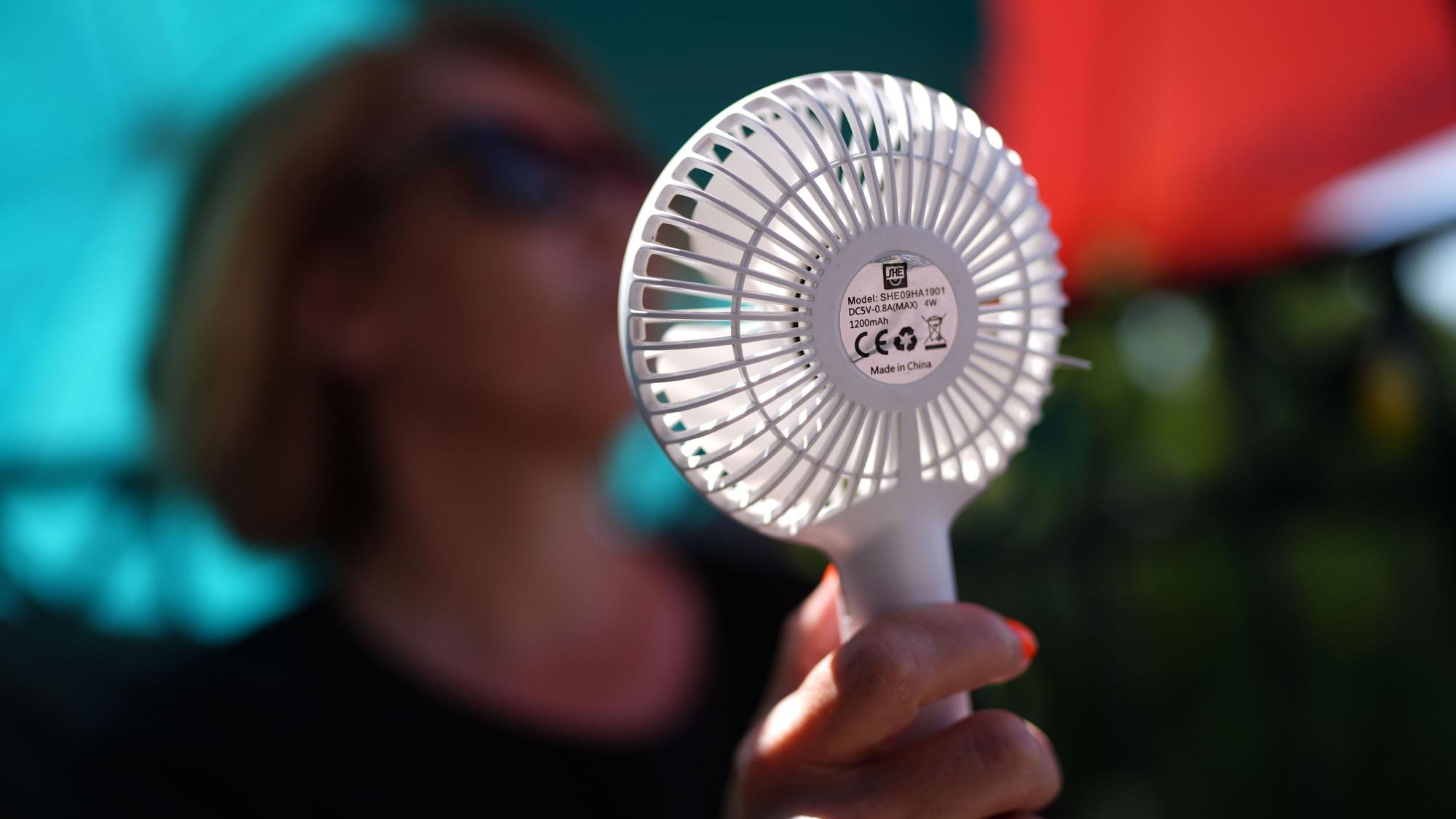 Eine Frau kühlt sich mit einem Handventilator unter Sonnenschirmen auf einem Balkon in der Mittagssonne ab. Die Hitzewelle in Deutschland sorgt aber auch nachts für schweißtreibende Temperaturen. (Symbolbild)