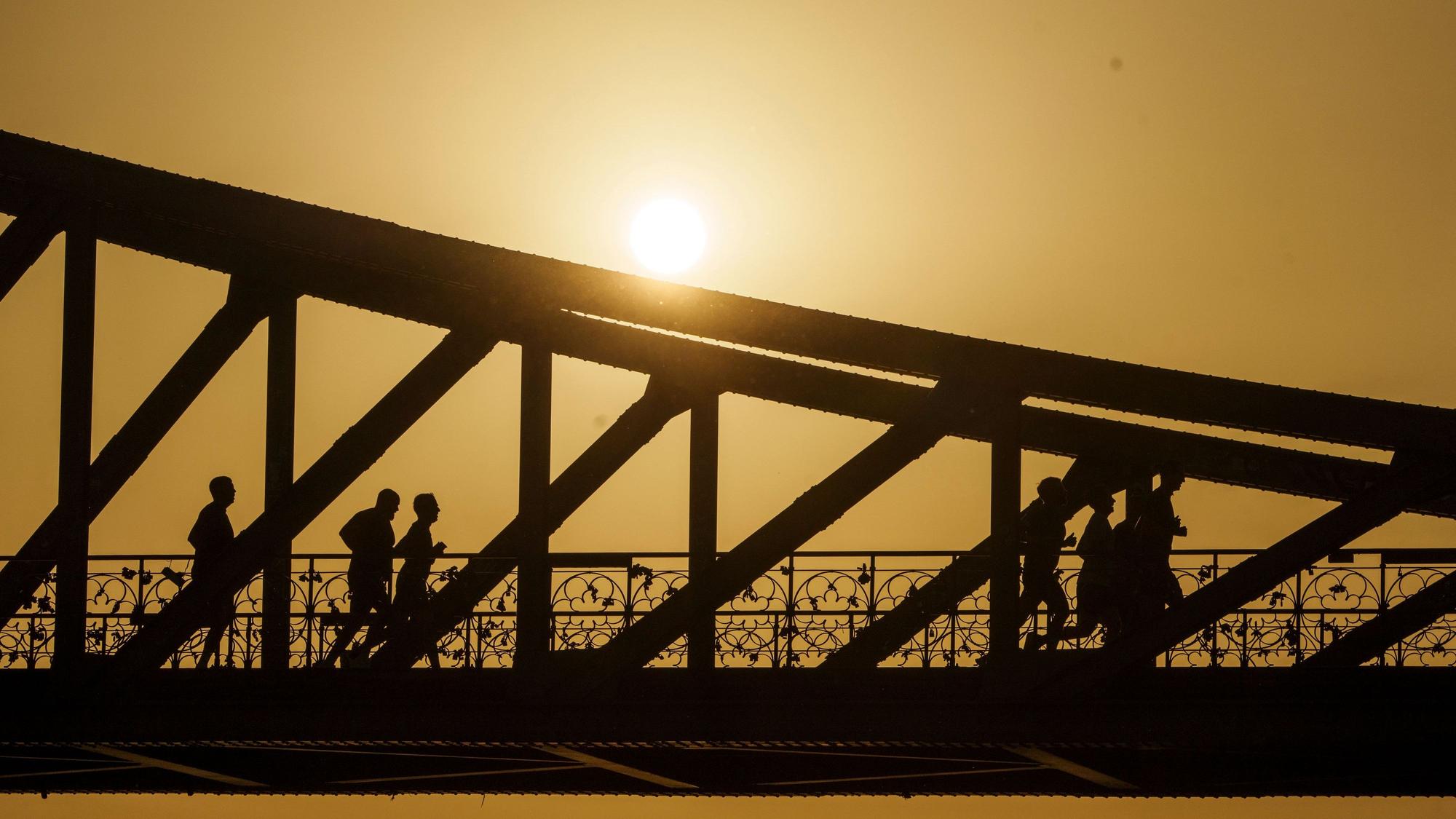 Eine Gruppe joggt bei Sonnenaufgang über den Eisernen Steg in Frankfurt am Main.
