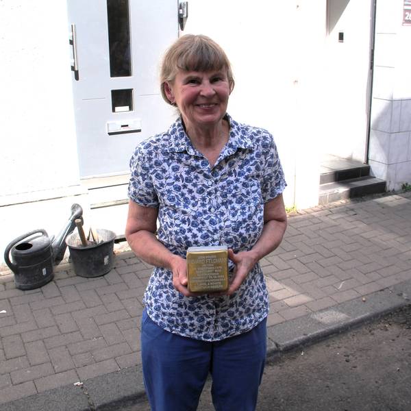 Eine Frau im geblümten Hemd hält einen Stolperstein in den Händen.