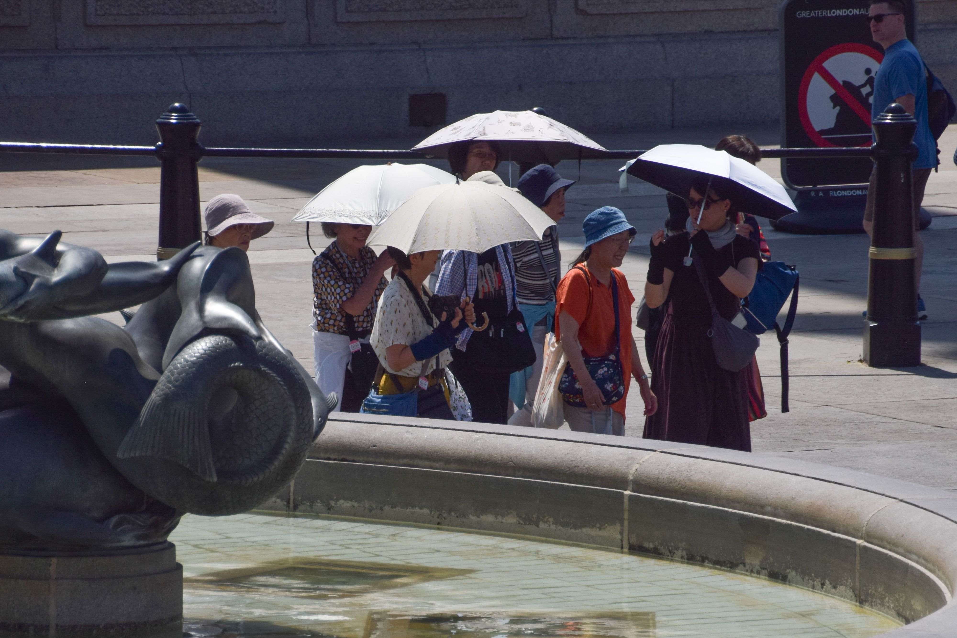 Auf dem Trafalgar Square suchen die Menschen unter Regenschirmen Schutz vor der Sonne.