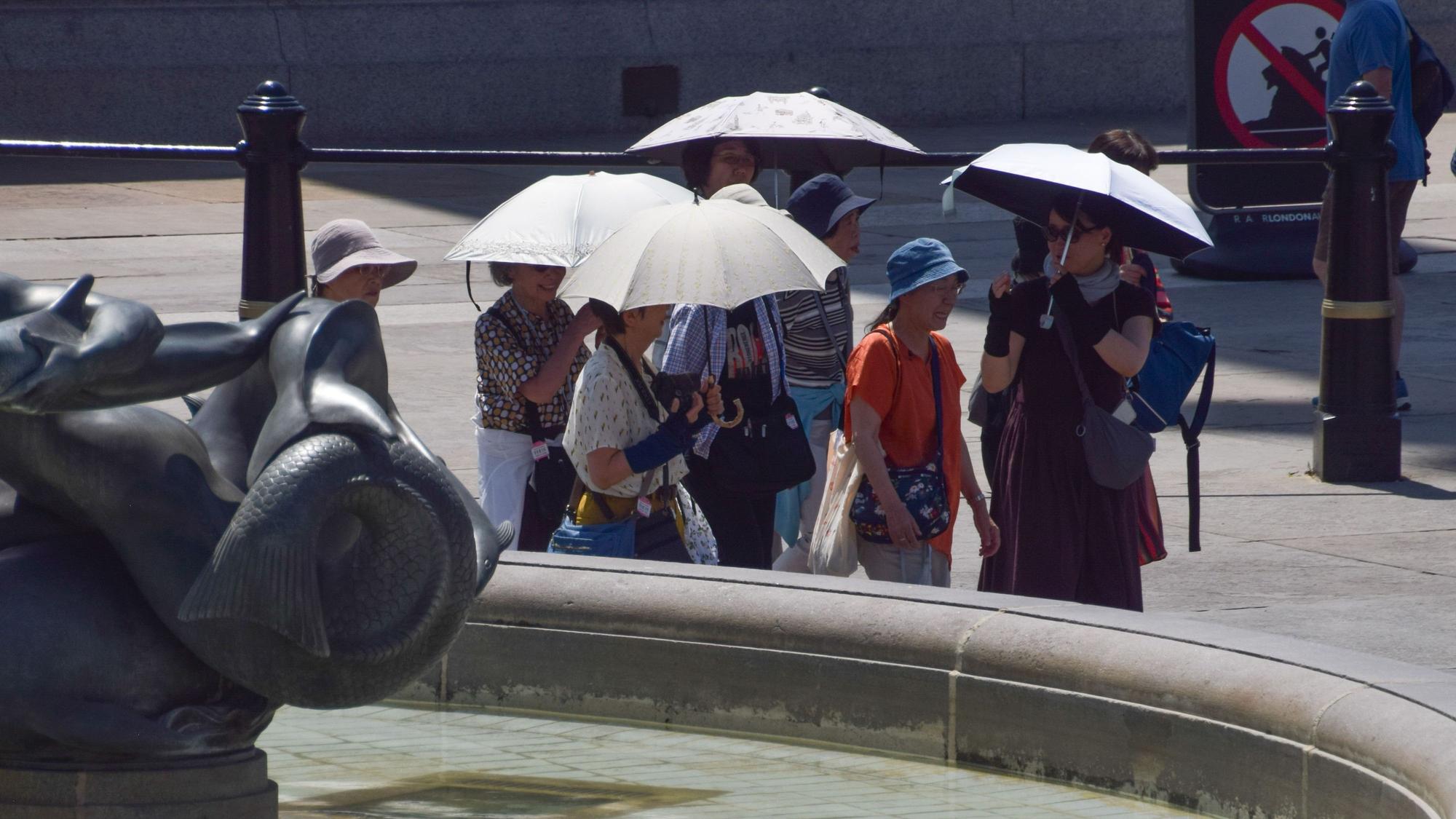 Auf dem Trafalgar Square suchen die Menschen unter Regenschirmen Schutz vor der Sonne.
