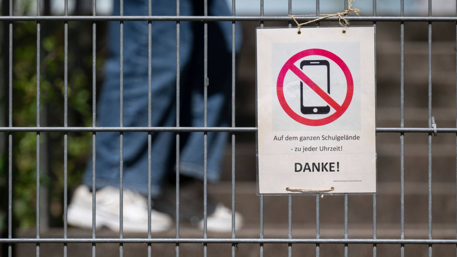 Ein Schild mit einem durchgestrichenen Smartphone und der Aufschrift „Auf dem ganzen Schulgelände – zu jeder Uhrzeit! DANKE!“ hängt am Zugangstor zum Schulhof eines Gymnasiums und weist auf ein generelles Handyverbot hin. Auch dazu hat Karin Prien konkrete Forderungen. (Archivbild)