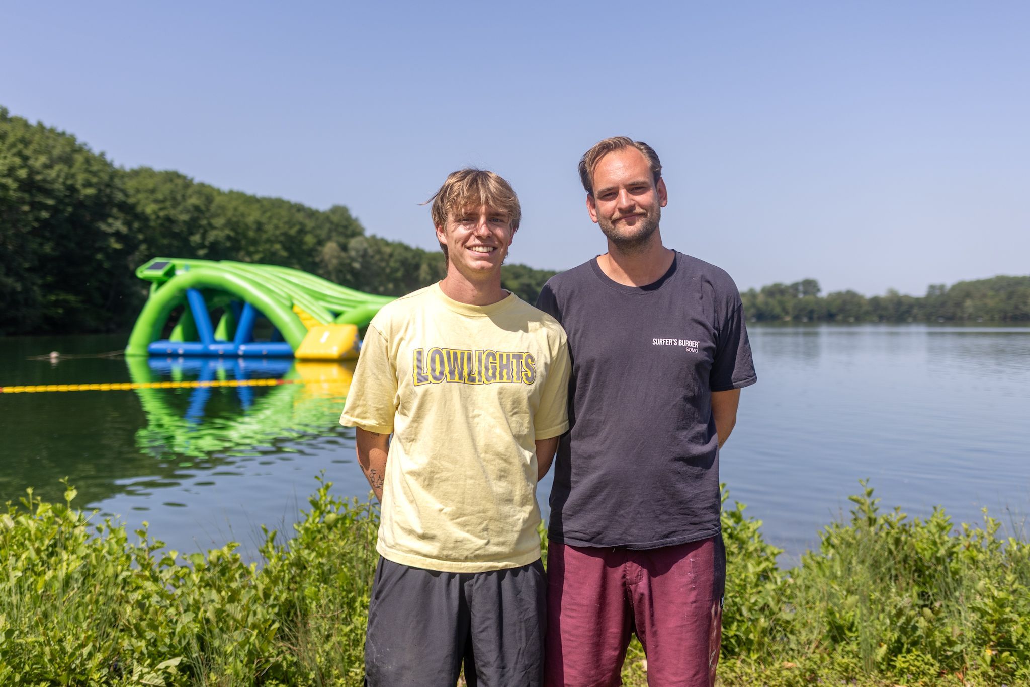 Zwei Männer stehen nebeneinander vor einem See und lächeln in die Kamera,