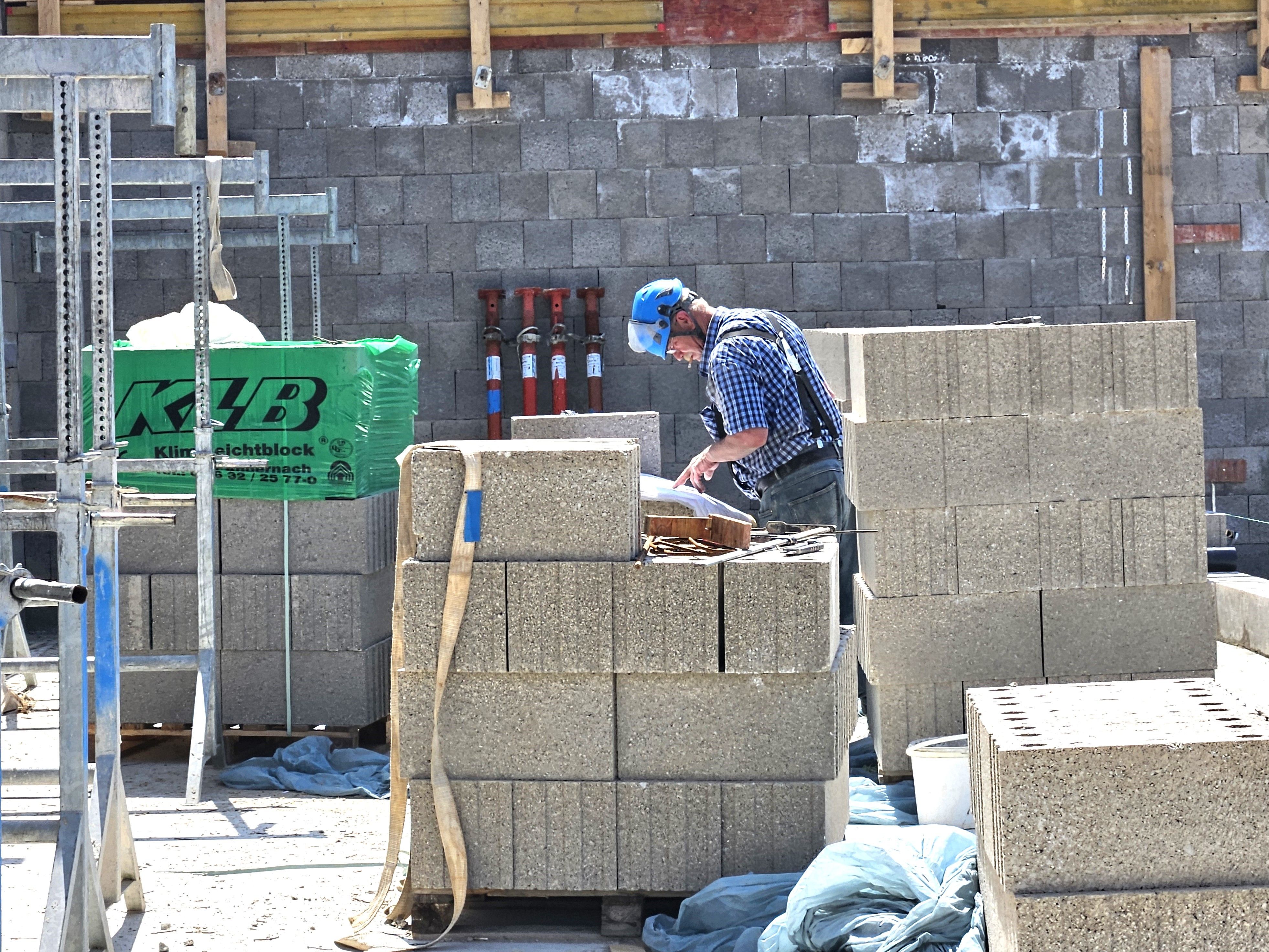 Ein Arbeiter mit Schutzhelm steht in einem Rohbau und studiert einen Bauplan.