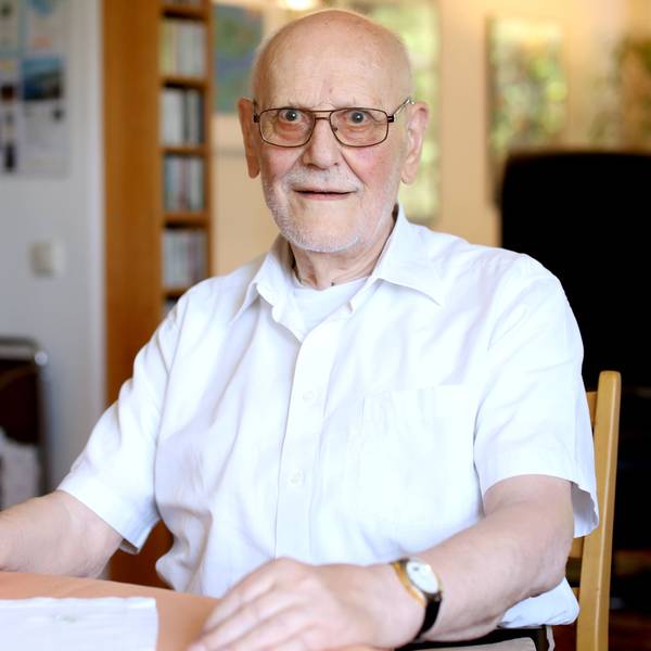 Werner Löwenstein sitzt an einem Tisch in seiner Wohnung und lächelt in die Kamera.