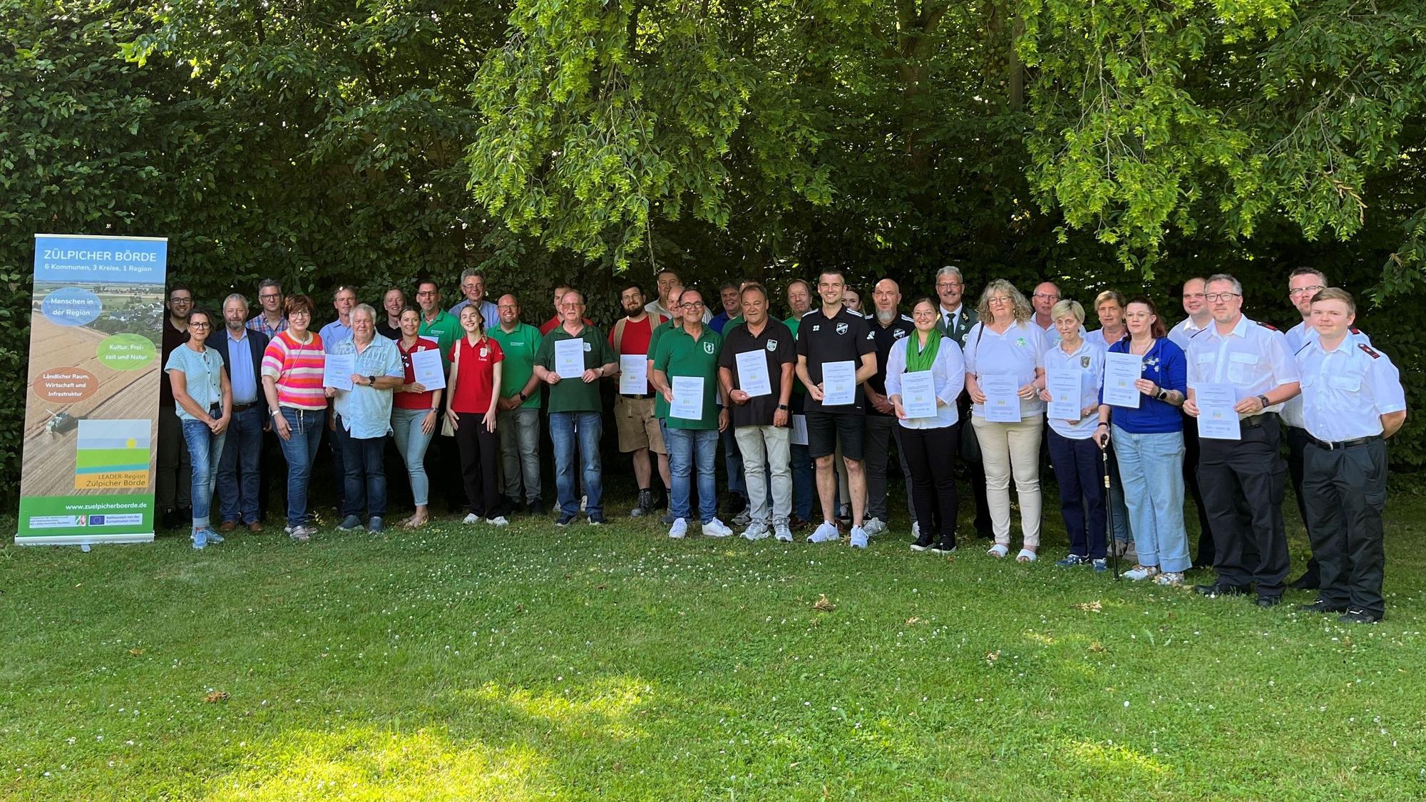 Die Vertreter der Verein stehen nebeneinander, einige halten Urkunden in den Häden. Links steht ein Banner der Leader-Region.
