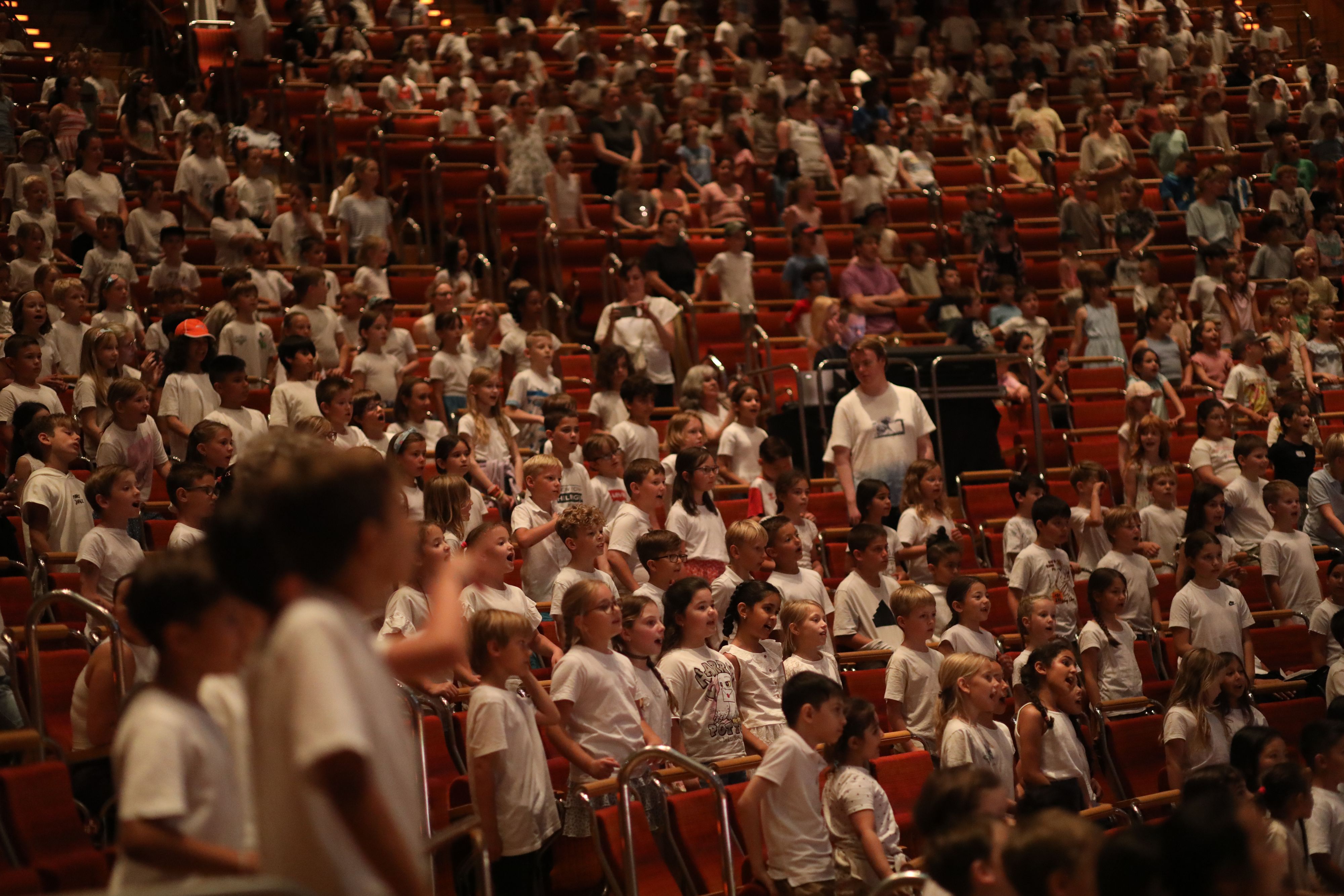 Die Ränge der Philharmonie mit vielen Kindern die stehen, singen und weiße Shirts tragen.