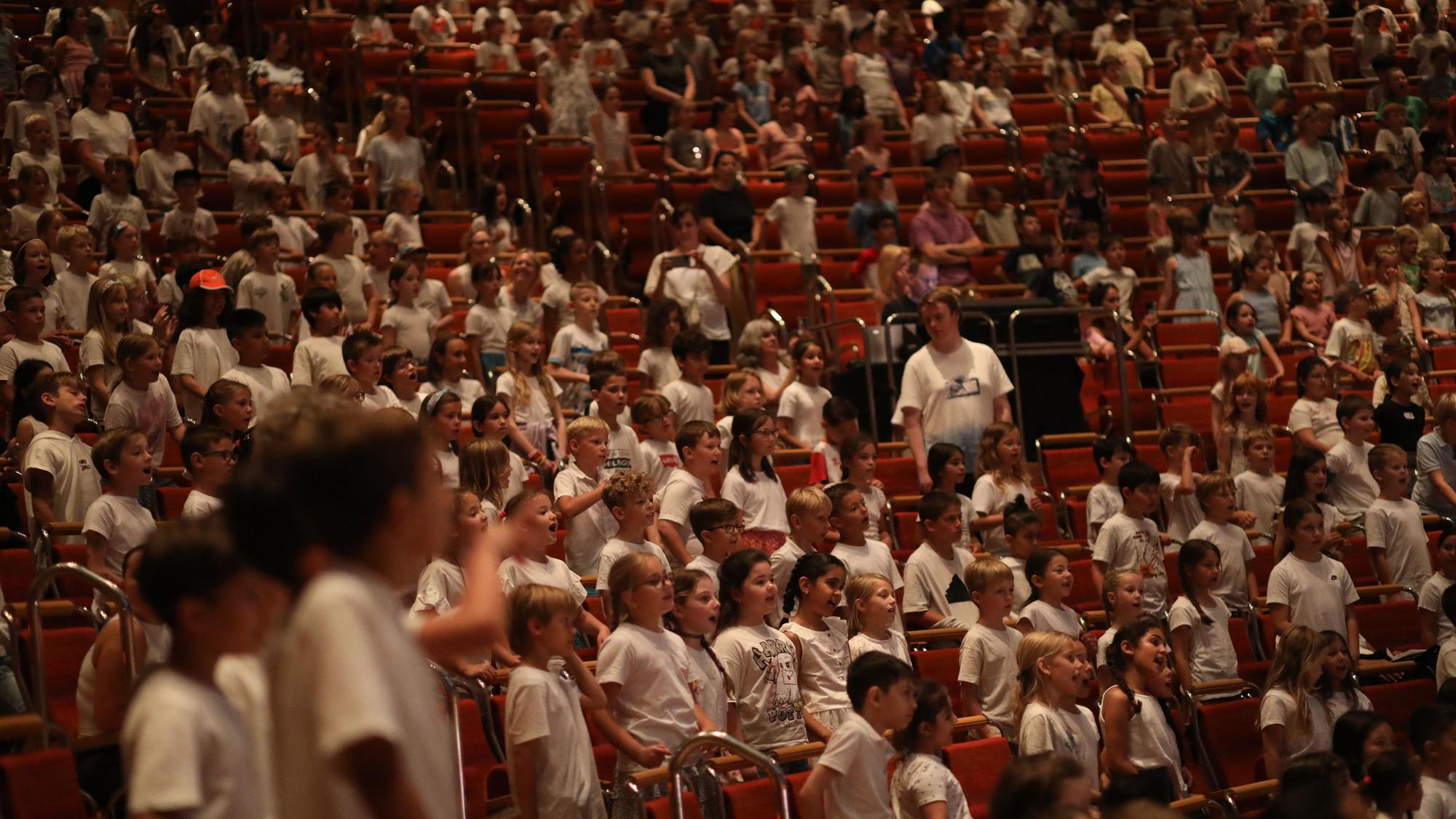 Die Ränge der Philharmonie mit vielen Kindern die stehen, singen und weiße Shirts tragen.