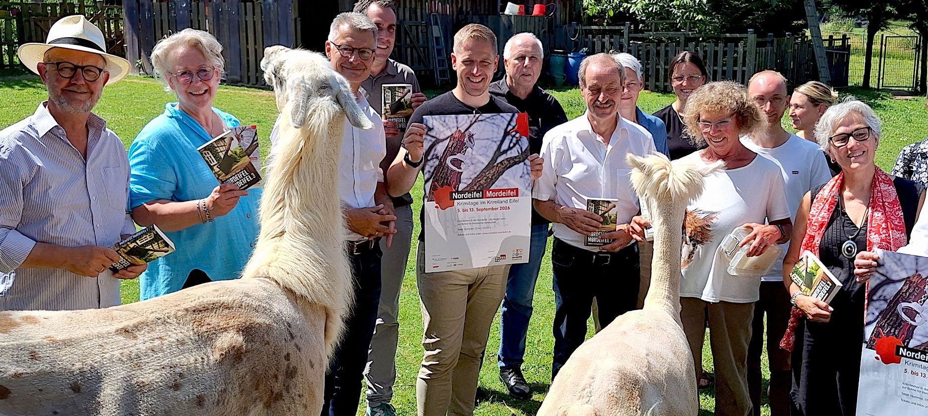 Ein Lama und ein Alpaka stehen im Vordergrund, dahinter sind Leute mit Büchern und Plakaten zu sehen.
