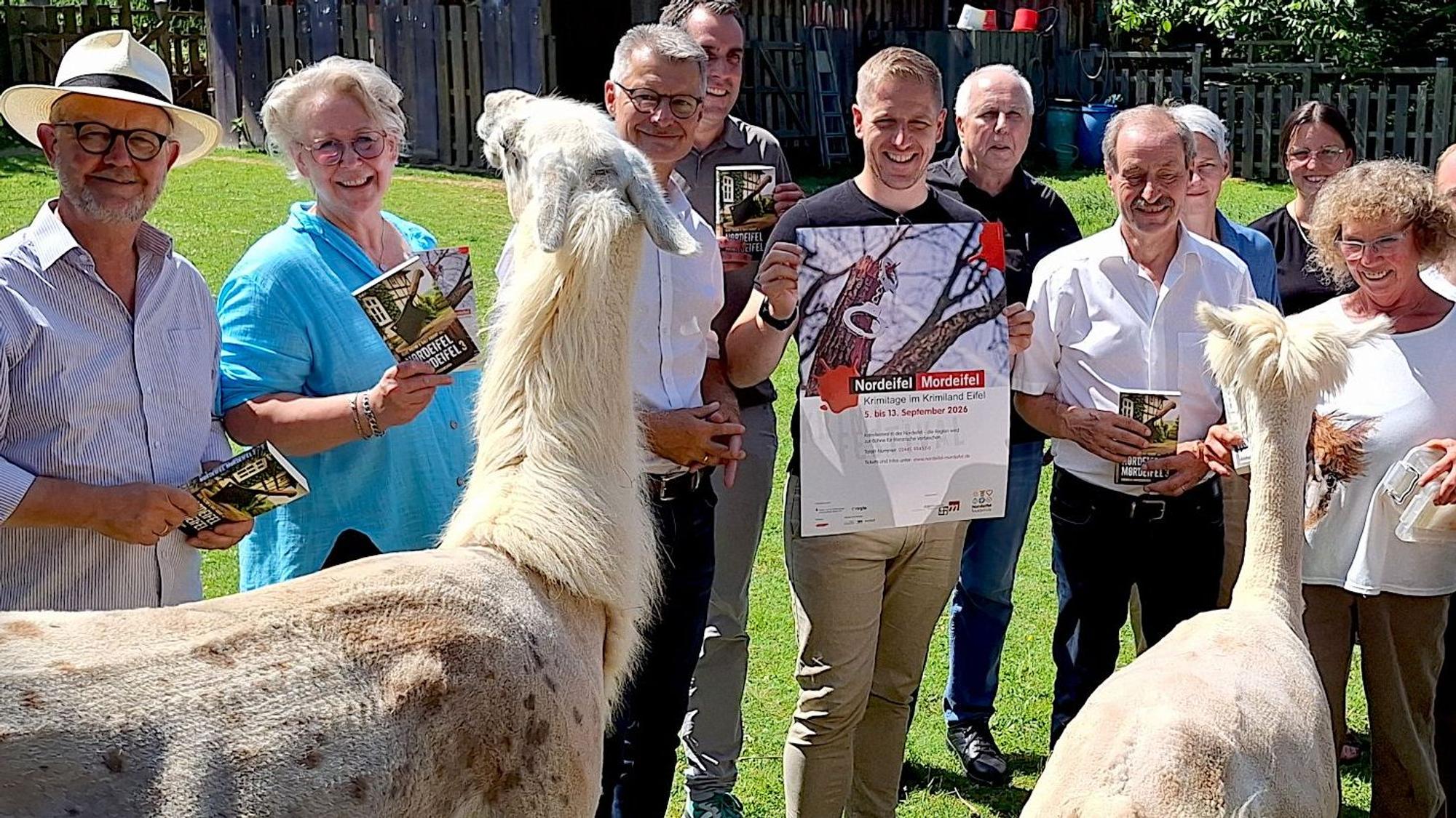 Ein Lama und ein Alpaka stehen im Vordergrund, dahinter sind Leute mit Büchern und Plakaten zu sehen.
