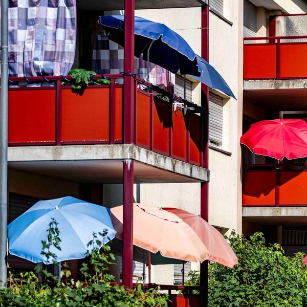 Das Bild zeigt zahlreiche Sonnenschirme, die auf Balkonen an einem Mehrfamilienhaus geöffnet worden sind.