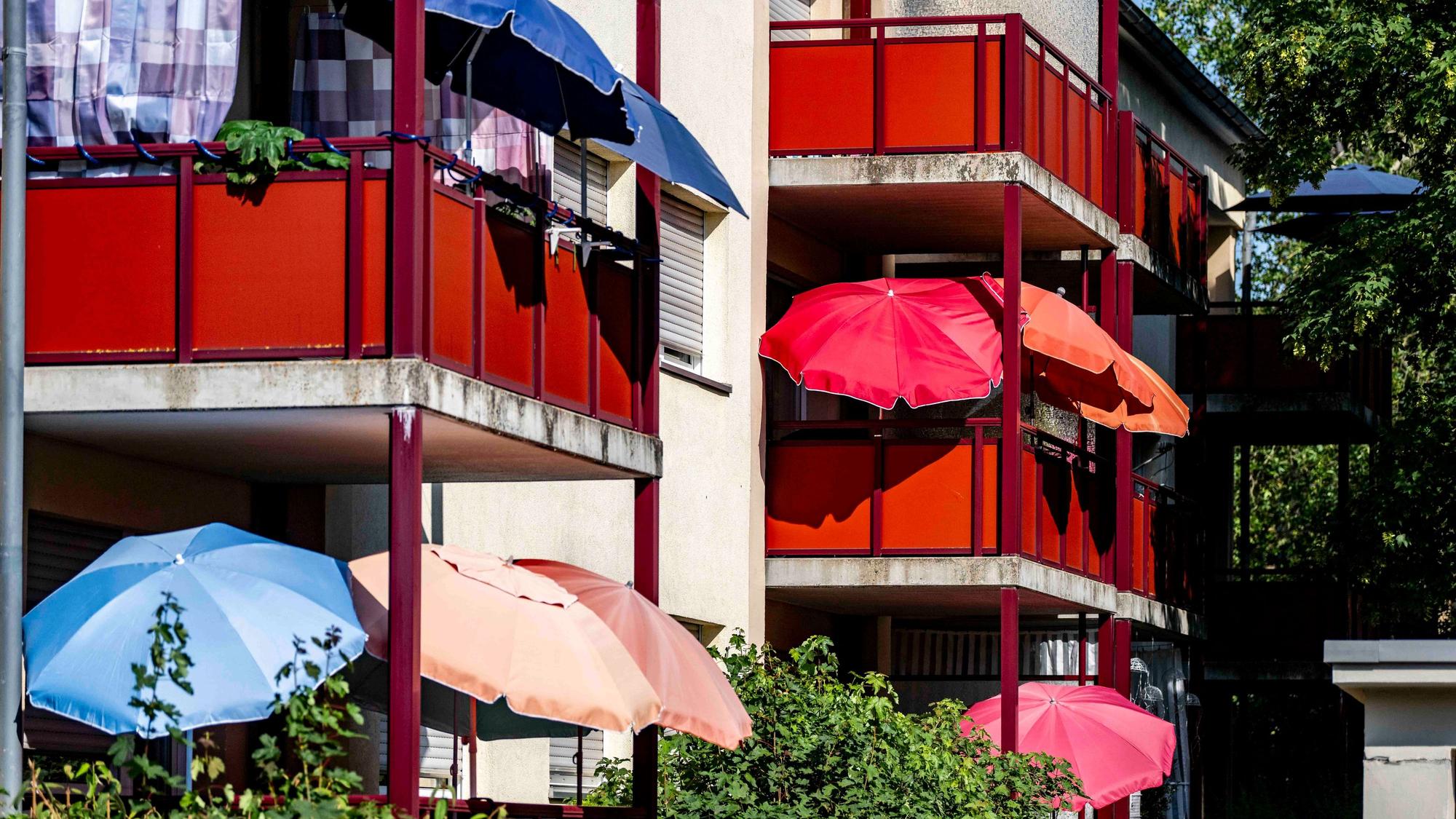 Das Bild zeigt zahlreiche Sonnenschirme, die auf Balkonen an einem Mehrfamilienhaus geöffnet worden sind.