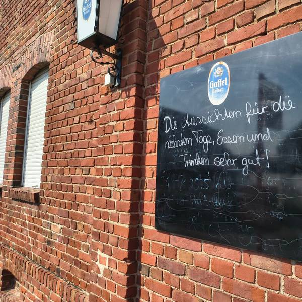 Auf einer Tafel an der Gaststätte in Köln-Langel werden Besucher noch herzlich empfangen. Bald schließt die Gastro in Rheinnähe.