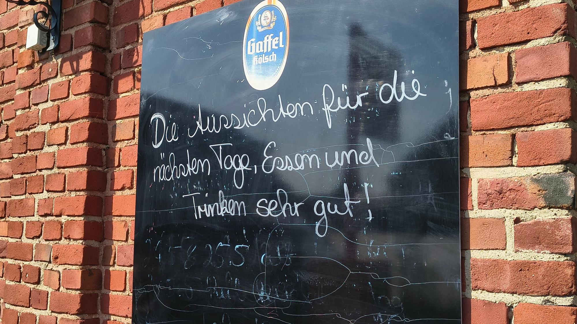 Auf einer Tafel an der Gaststätte in Köln-Langel werden Besucher noch herzlich empfangen. Bald schließt die Gastro in Rheinnähe.