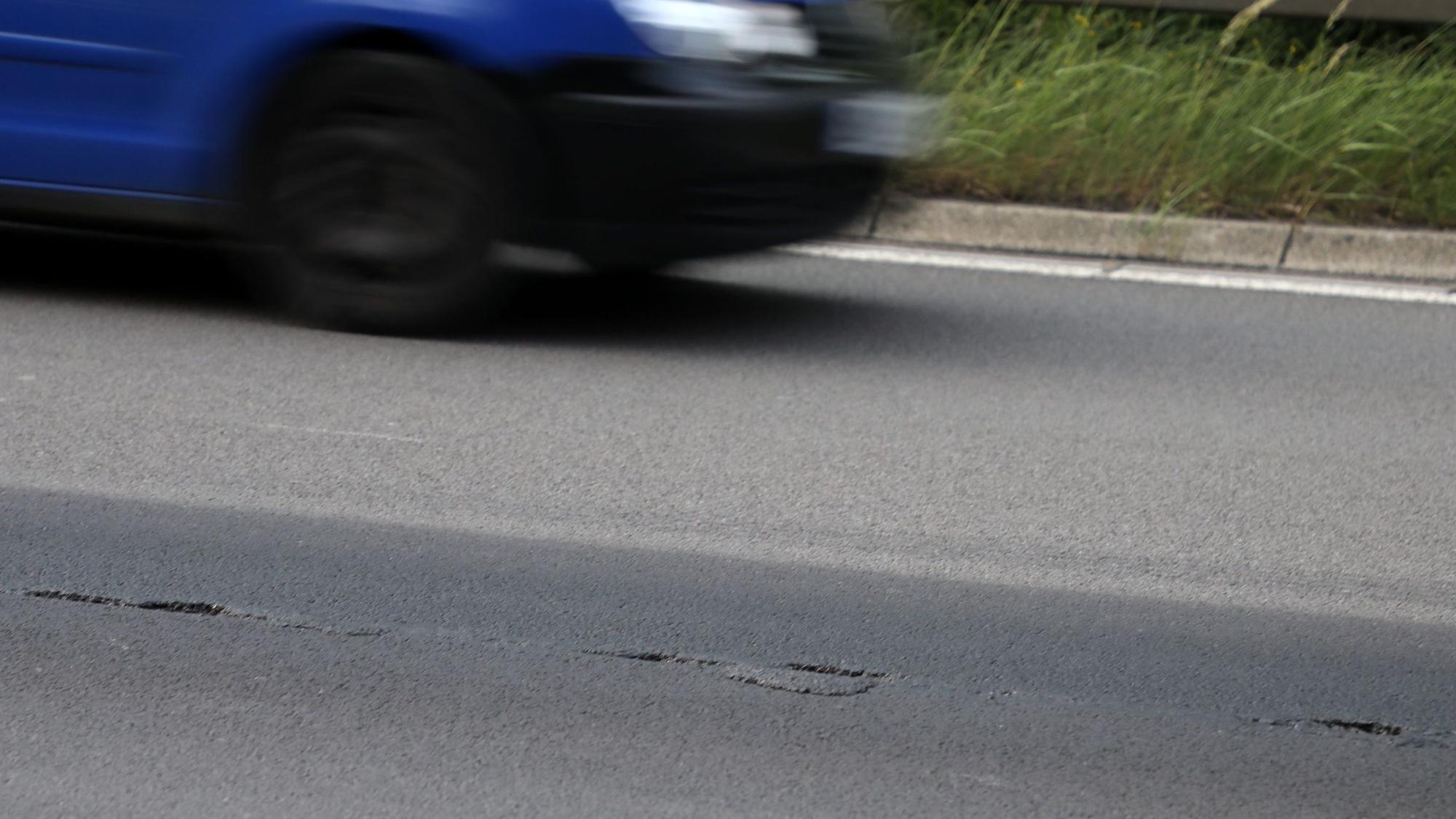 Eine Asphaltfahrbahn reißt auf, im Hintergrund fährt ein Auto vorbei.