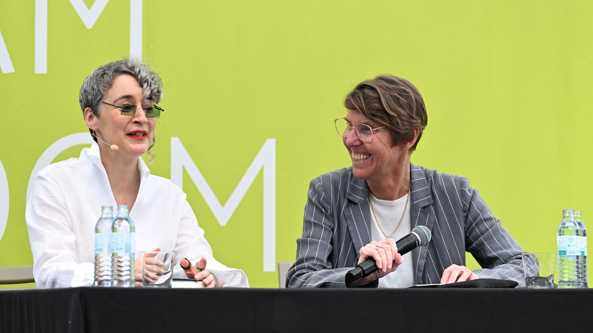 Die beiden Frauen sitzen nebeneinander auf dem Podium.