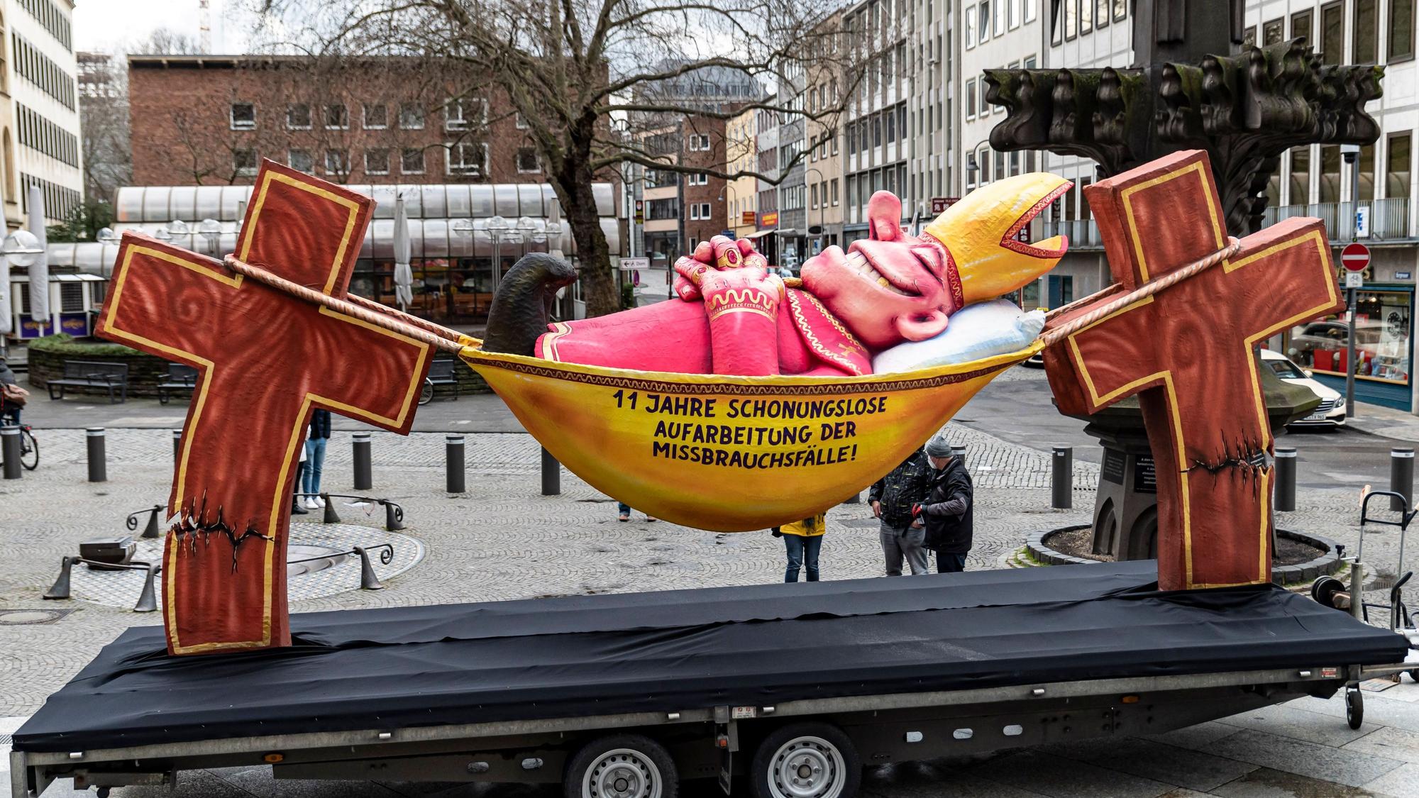 Die Plastik des Düsseldorfer Künstlers Jacques Tilly mit dem Slogan „11 Jahre schonungslose Aufarbeitung der Missbrauchsfälle" steht im März 2021 vor dem Kölner Dom in der Kölner Altstadt.