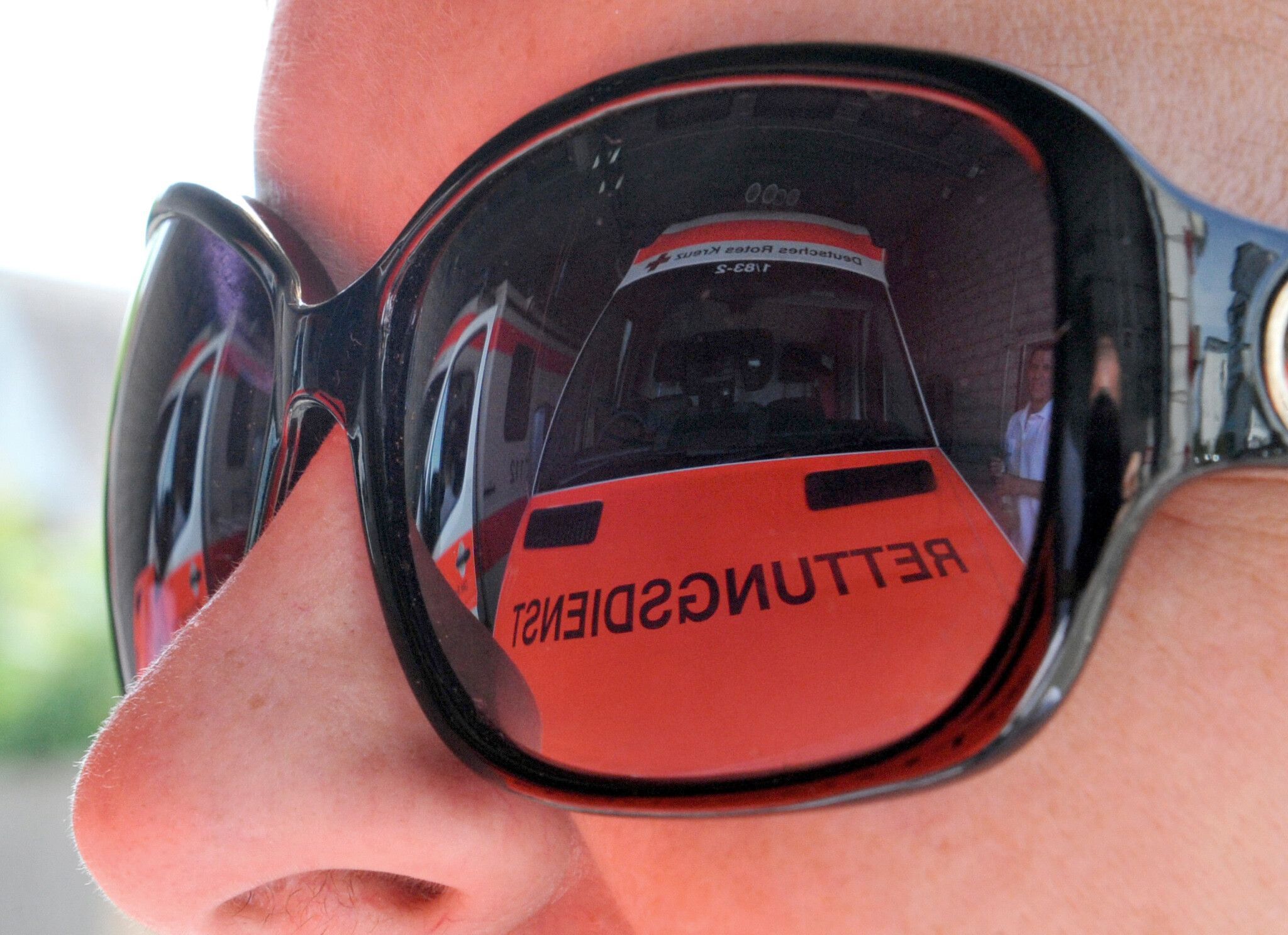 Ein Rettungswagen spiegelt sich in der Sonnenbrille einer Rettungsassistentin.