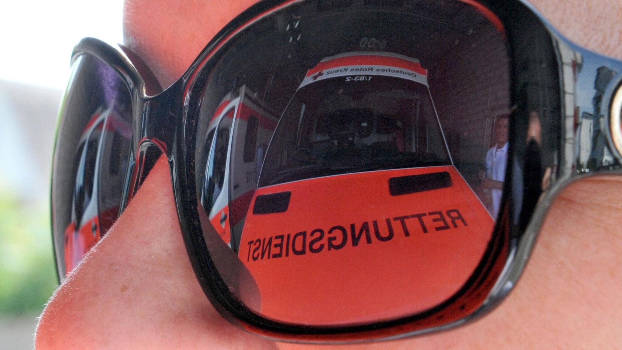 Ein Rettungswagen spiegelt sich in der Sonnenbrille einer Rettungsassistentin.