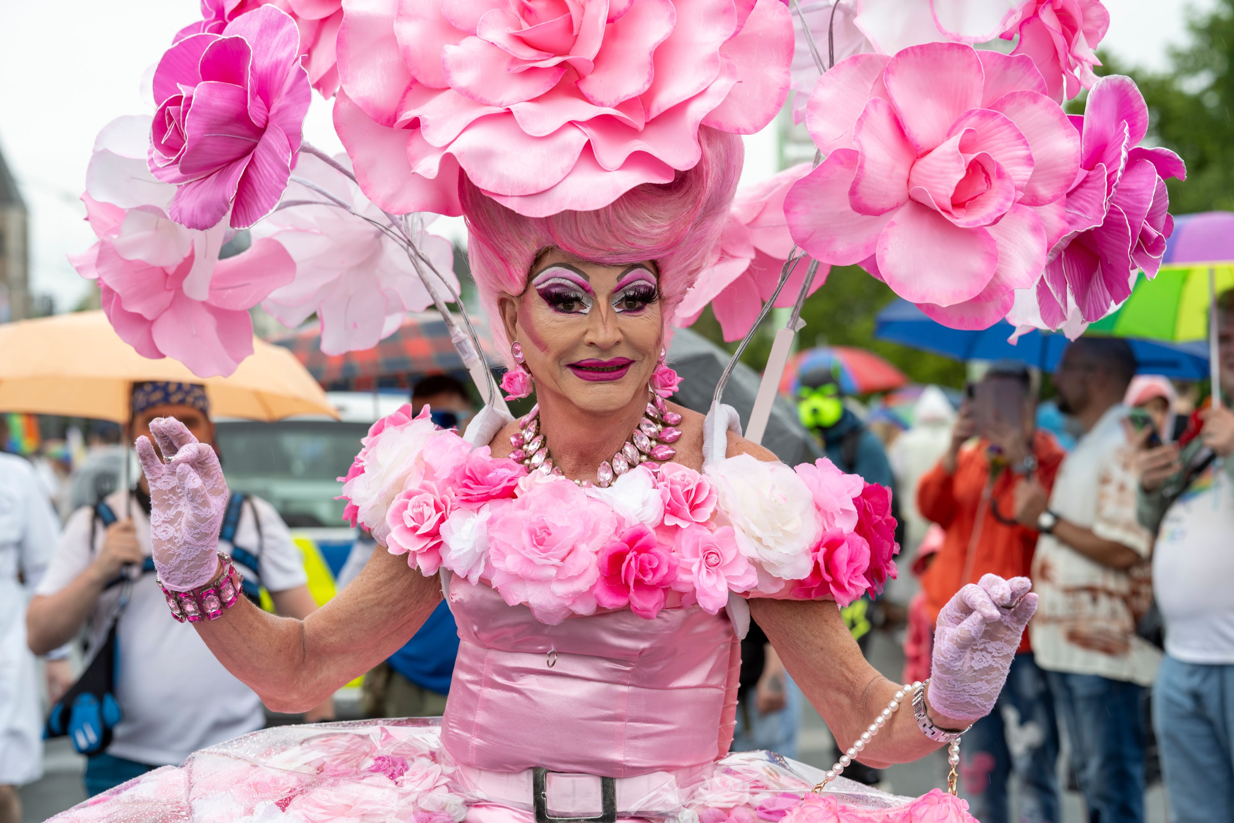 Eine Drag Queen in einem rosaroten Blumenkostüm schaut in die Kamera.