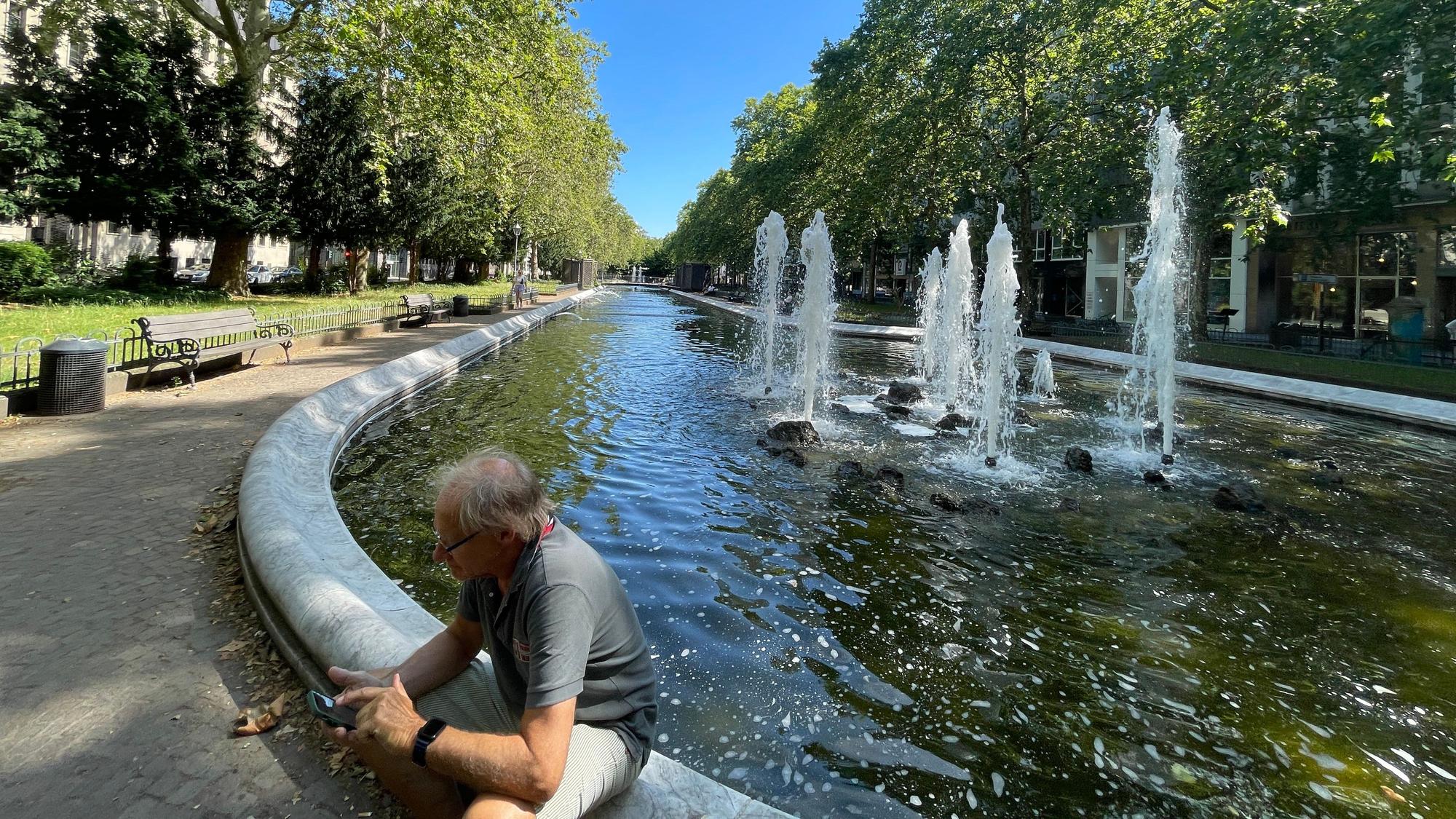 Ein Mann sitzt am Rand des Springbrunnens am Kaiser-Wilhelm-Ring.